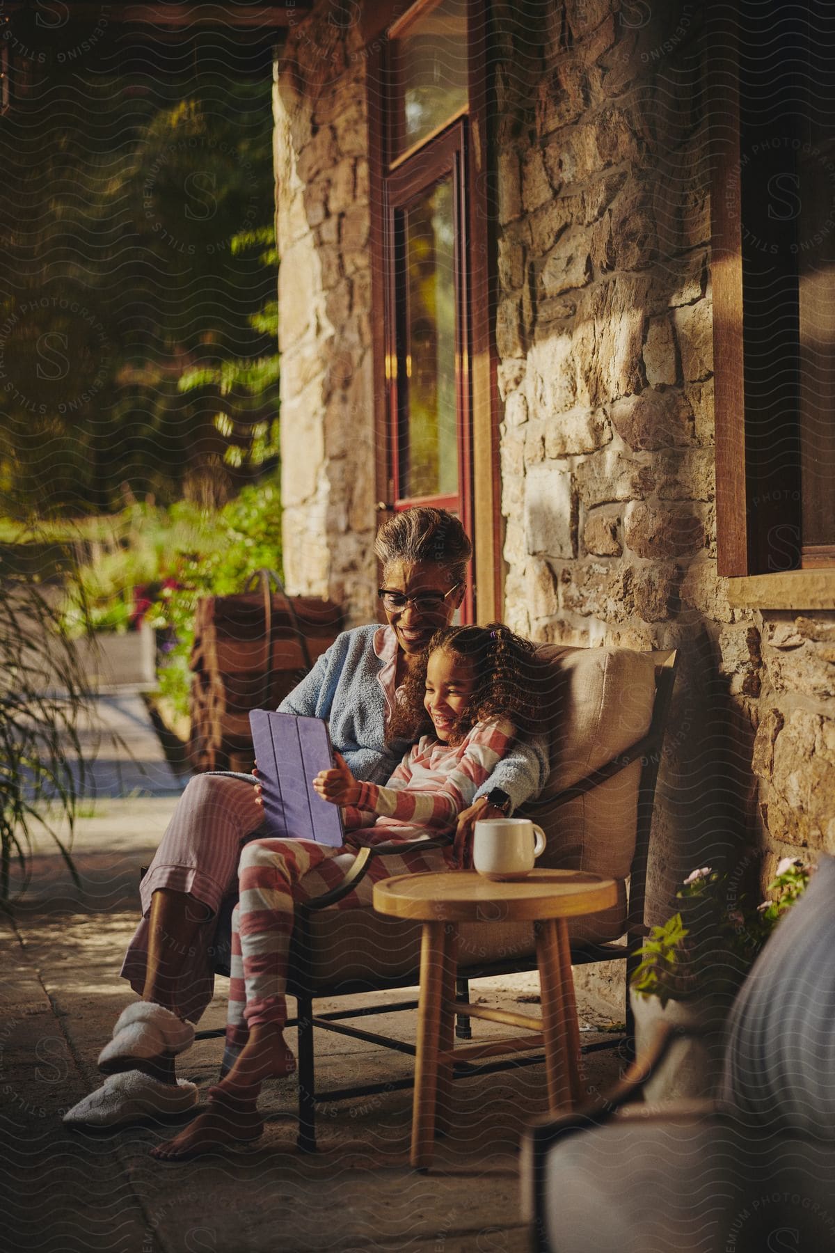 A little girl is sitting outside on the patio with a laptop computer as her mother sits next to her and they smile