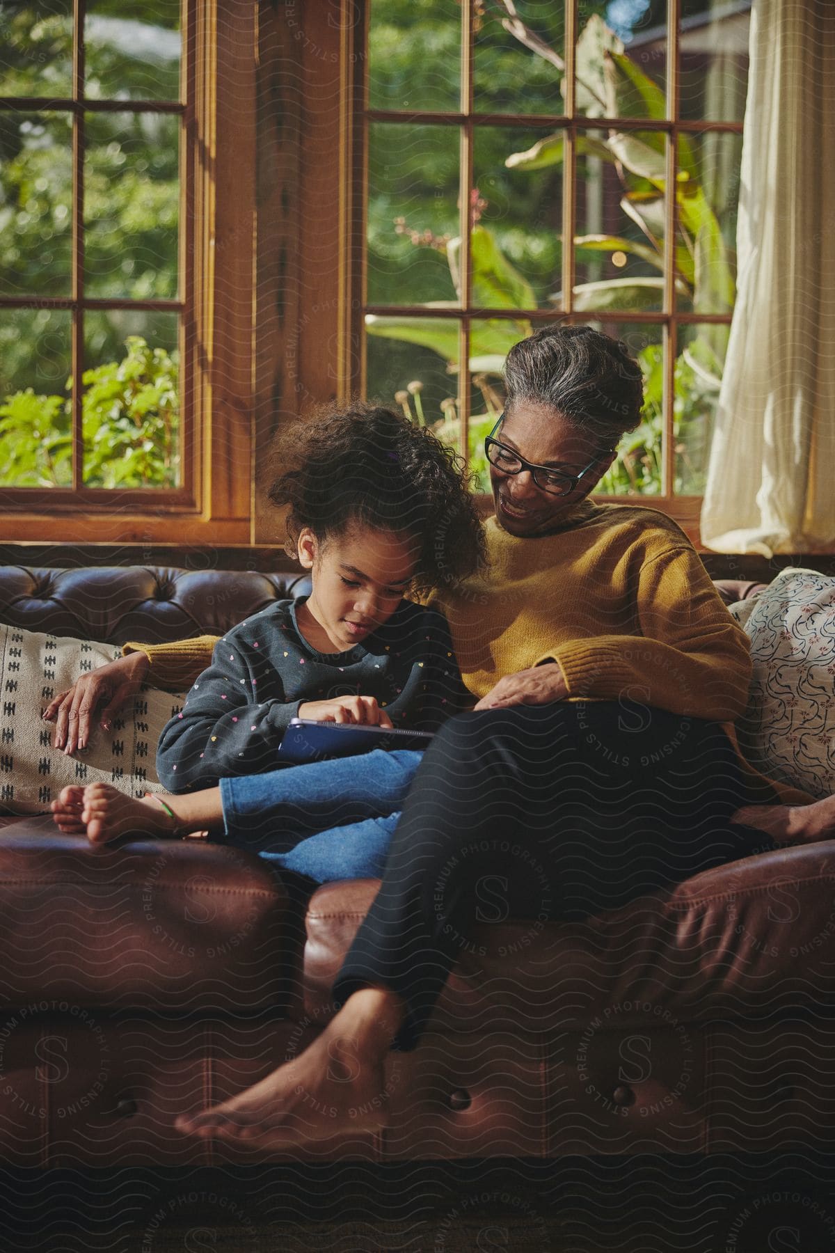 A woman sits on the living room couch with her young daughter as they look at a tablet computer