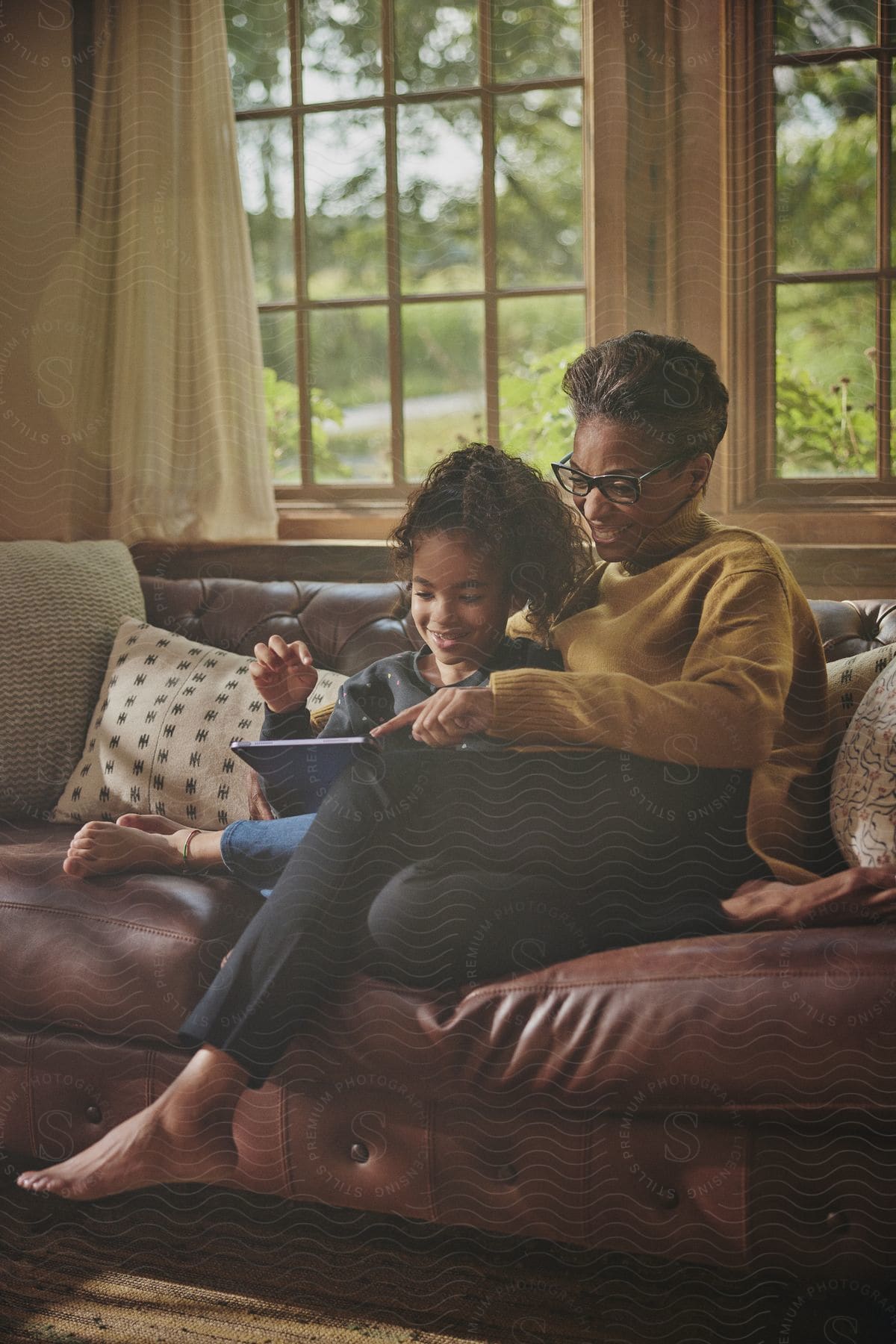 A woman sits on the living room couch with her granddaughter as they look at a tablet computer