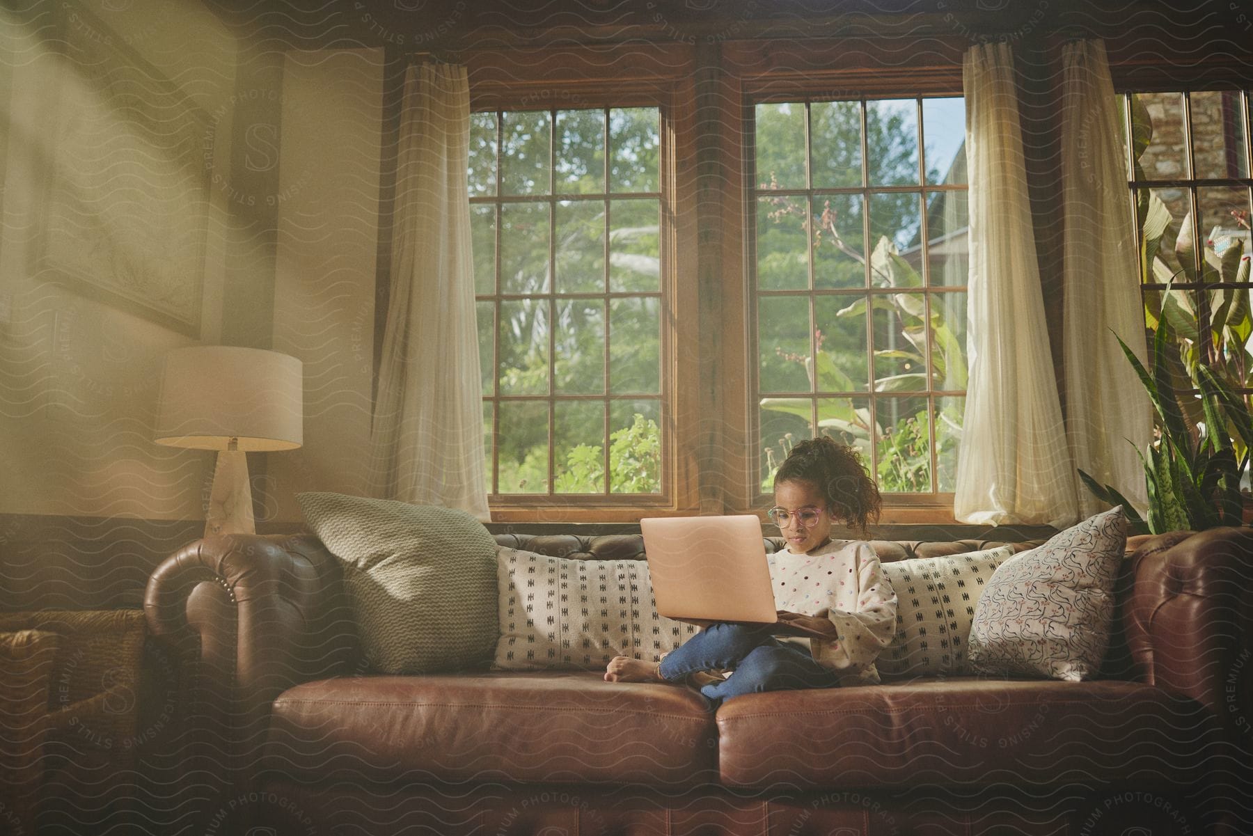 A young girl is sitting on the living room couch with a laptop computer