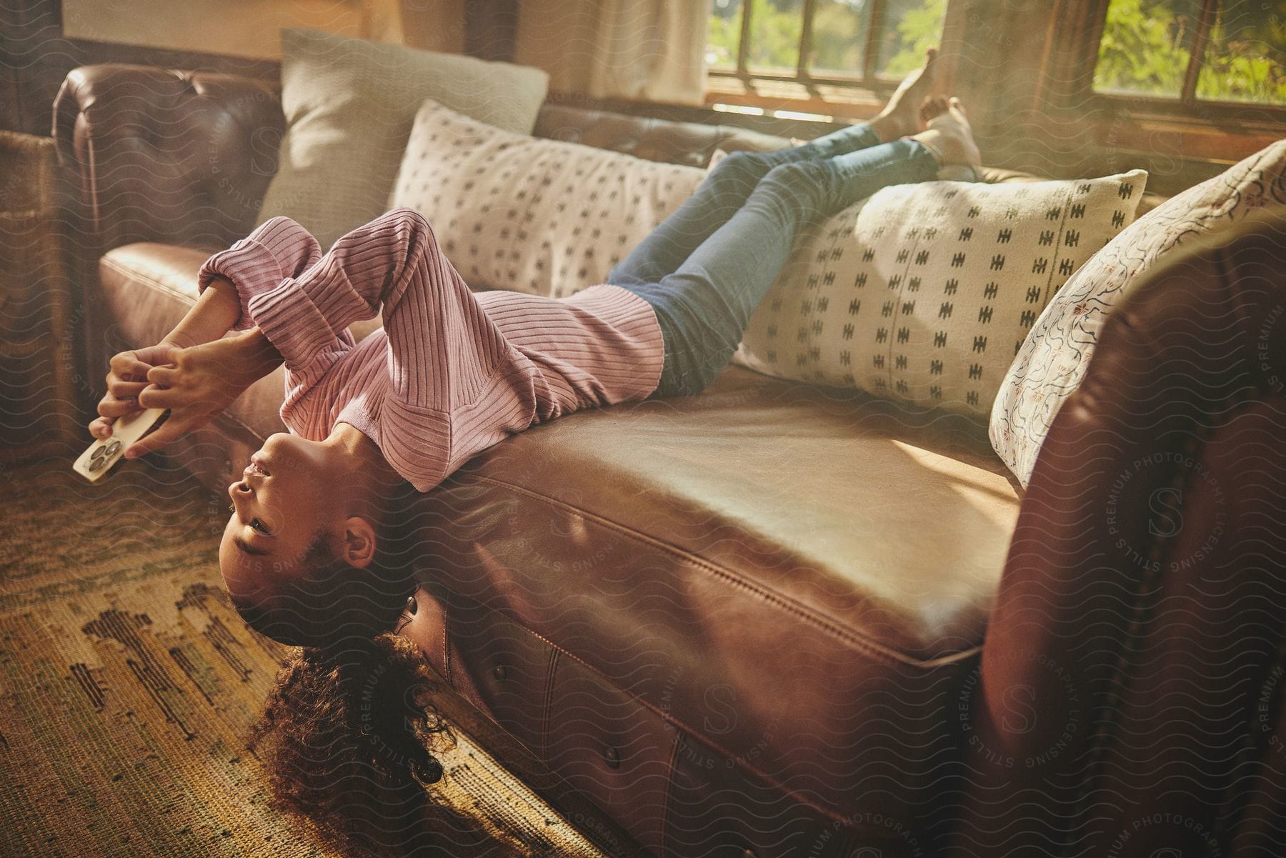 A young girl lies on her back on a sofa while looking at her smartphone.