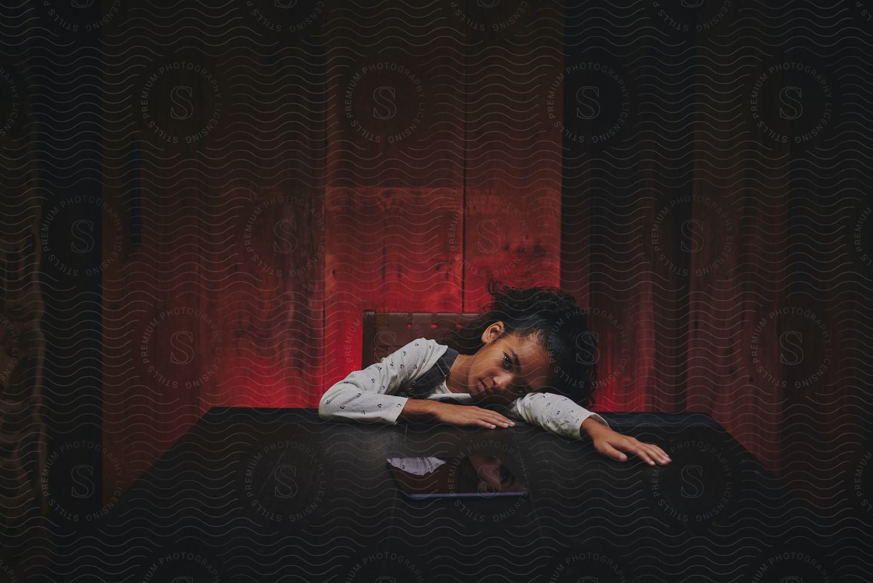 A young girl is sitting at a table and her head down resting on her arm with a tablet computer in front of her