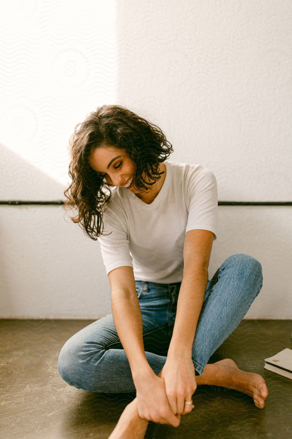 A woman in jeans and white shirt laughs while sitting on the floor.