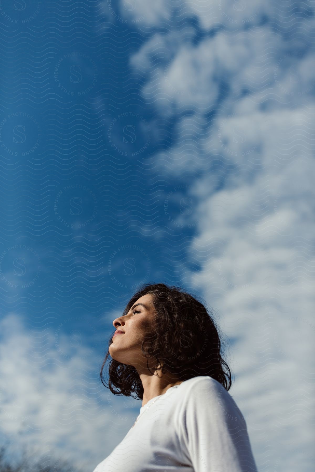 Sun shines on a young woman's face as she stands outside under a cloudy sky