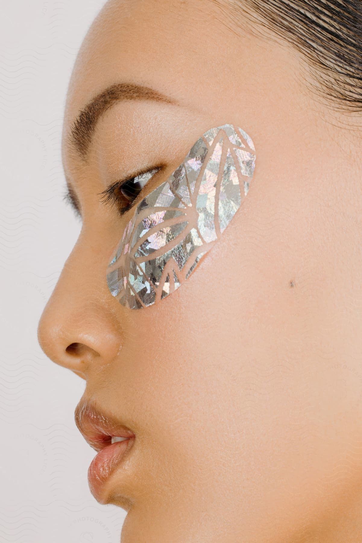 A young woman looks sideways with a metallic decoration on her cheek