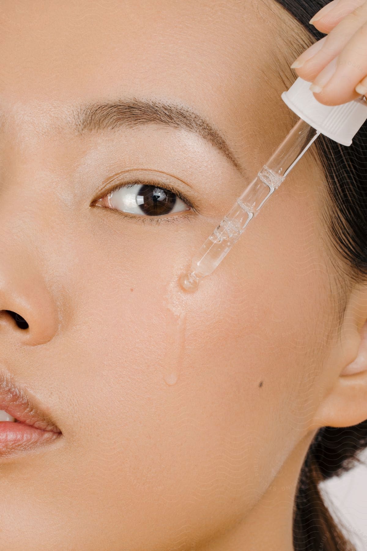 A young woman applies a skincare product to her cheek using a dropper.