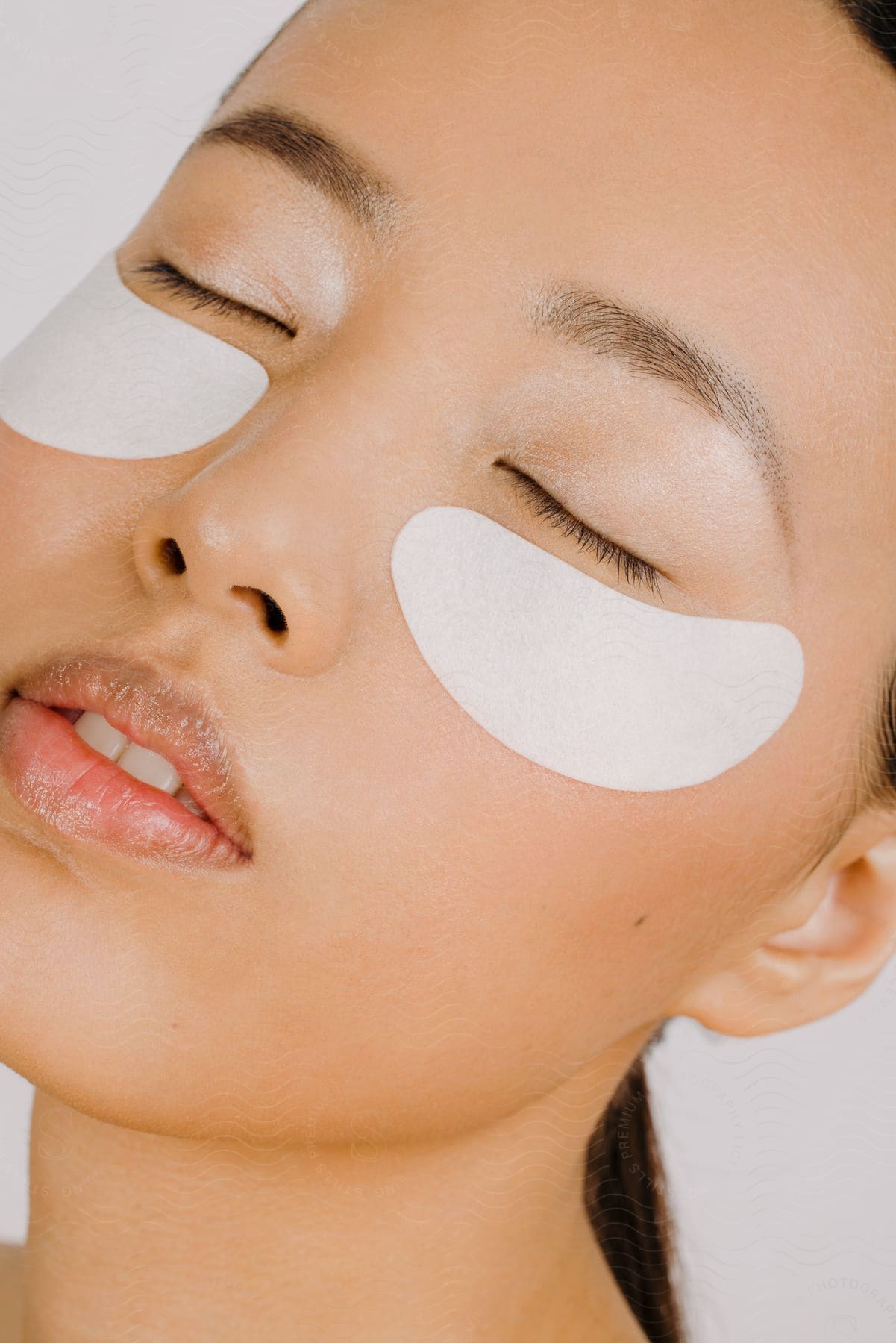 An Asian woman woman with eyes closed and skin treatment strips on her cheeks.