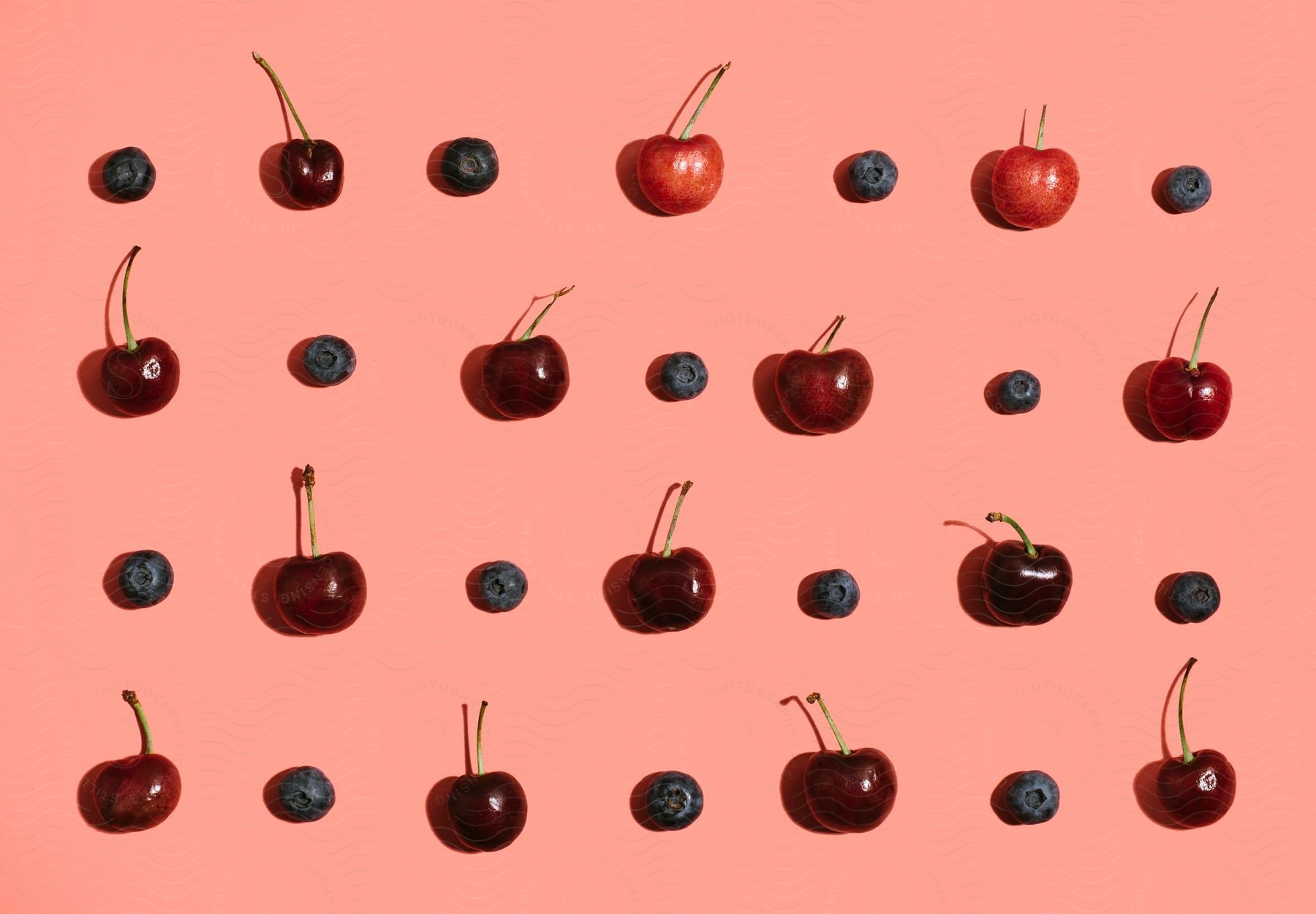 Cherries and blueberries are placed in a pattern on a pink background.