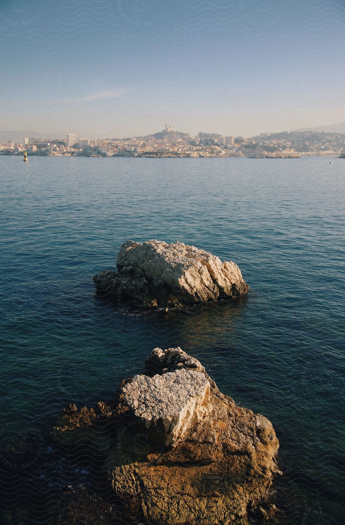 Two rocks in the water with a distant city skyline over the sea.