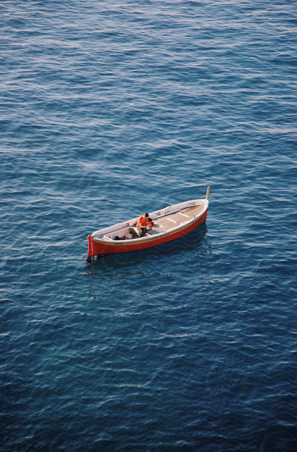 Man sits in red boat floating on water surface.