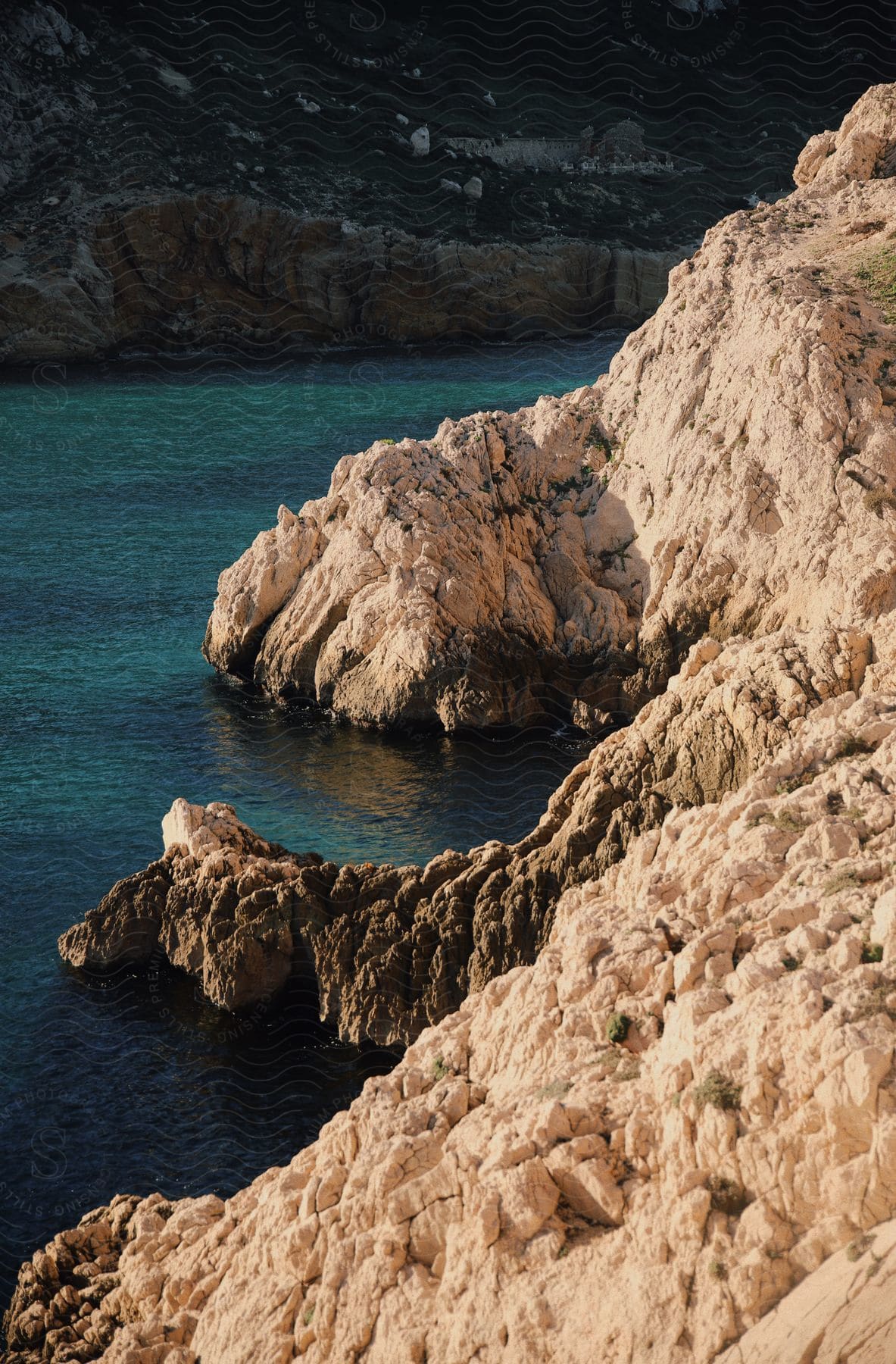 Rocky coastline with jagged cliffs overlooking turquoise waters, with a distant view of a hillside.