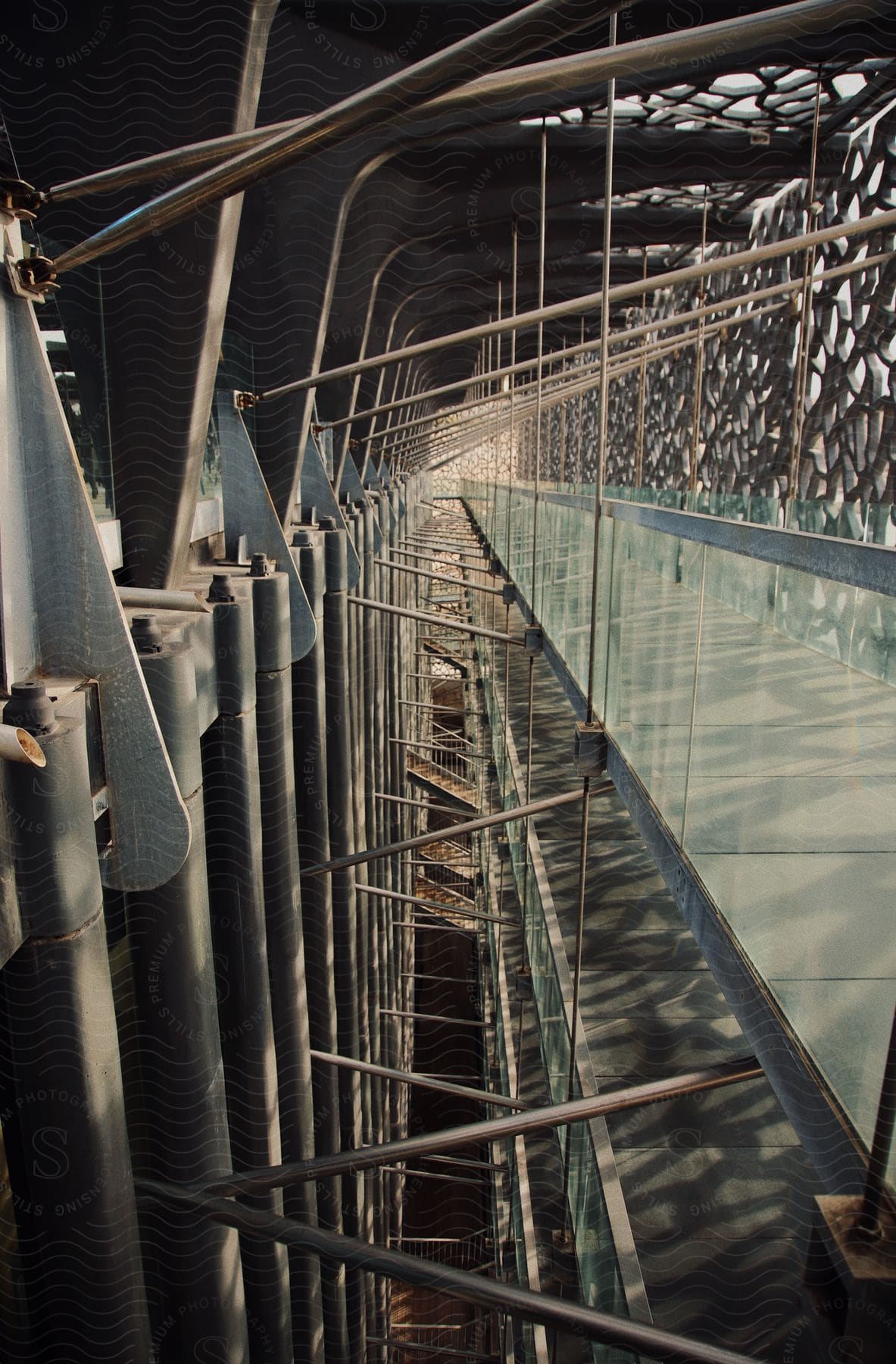 Interior perspective of a modern structure with metal railings and geometric patterned panels, creating shadows on the walkway.