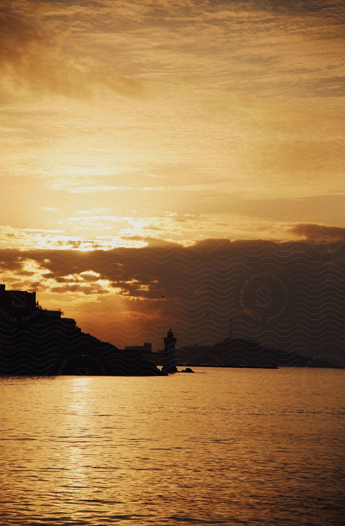 A landscape of a lighthouse on the coast silhouetted against the sunset.