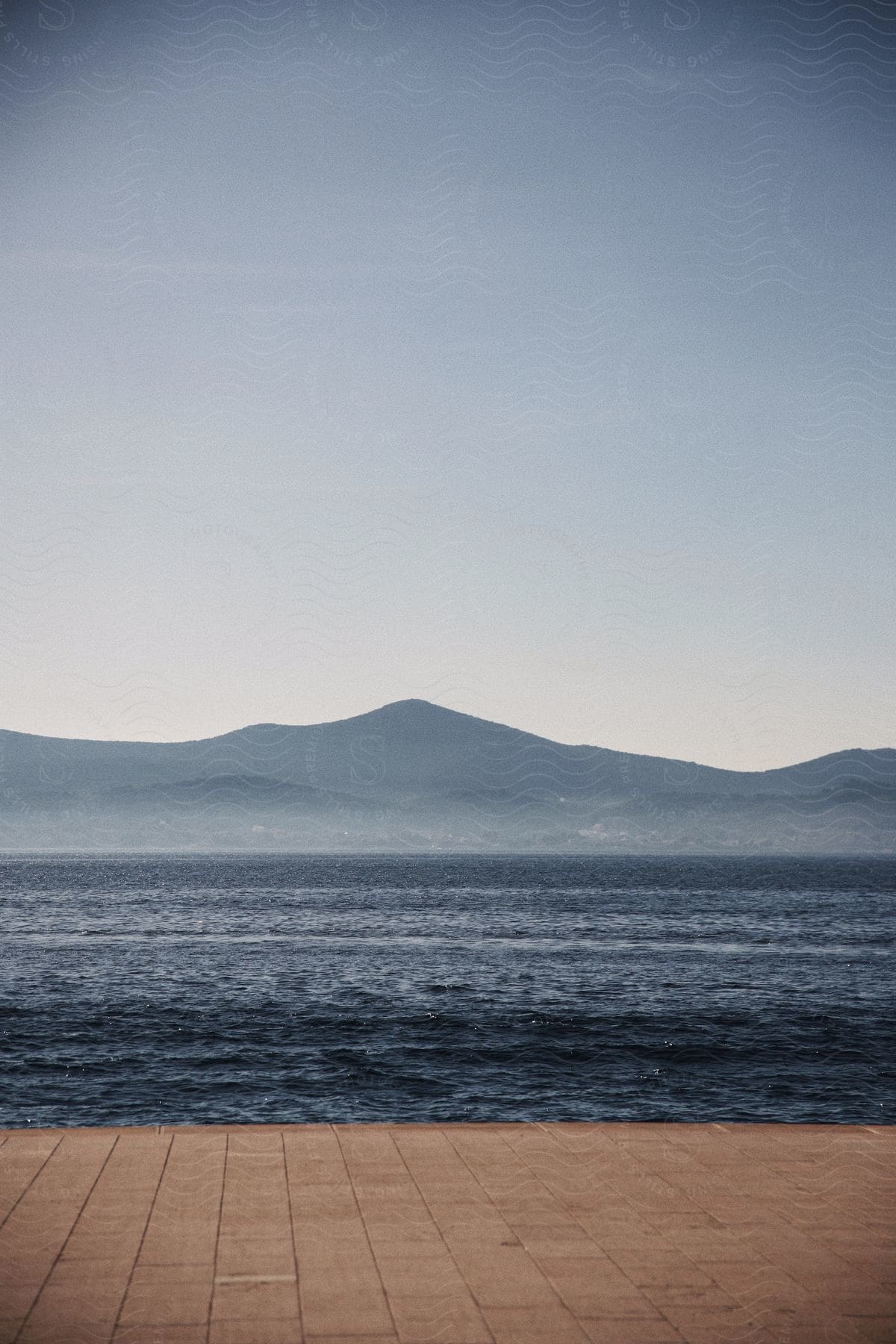 Waves roll in along the coast with mountains in the distance under a hazy sky