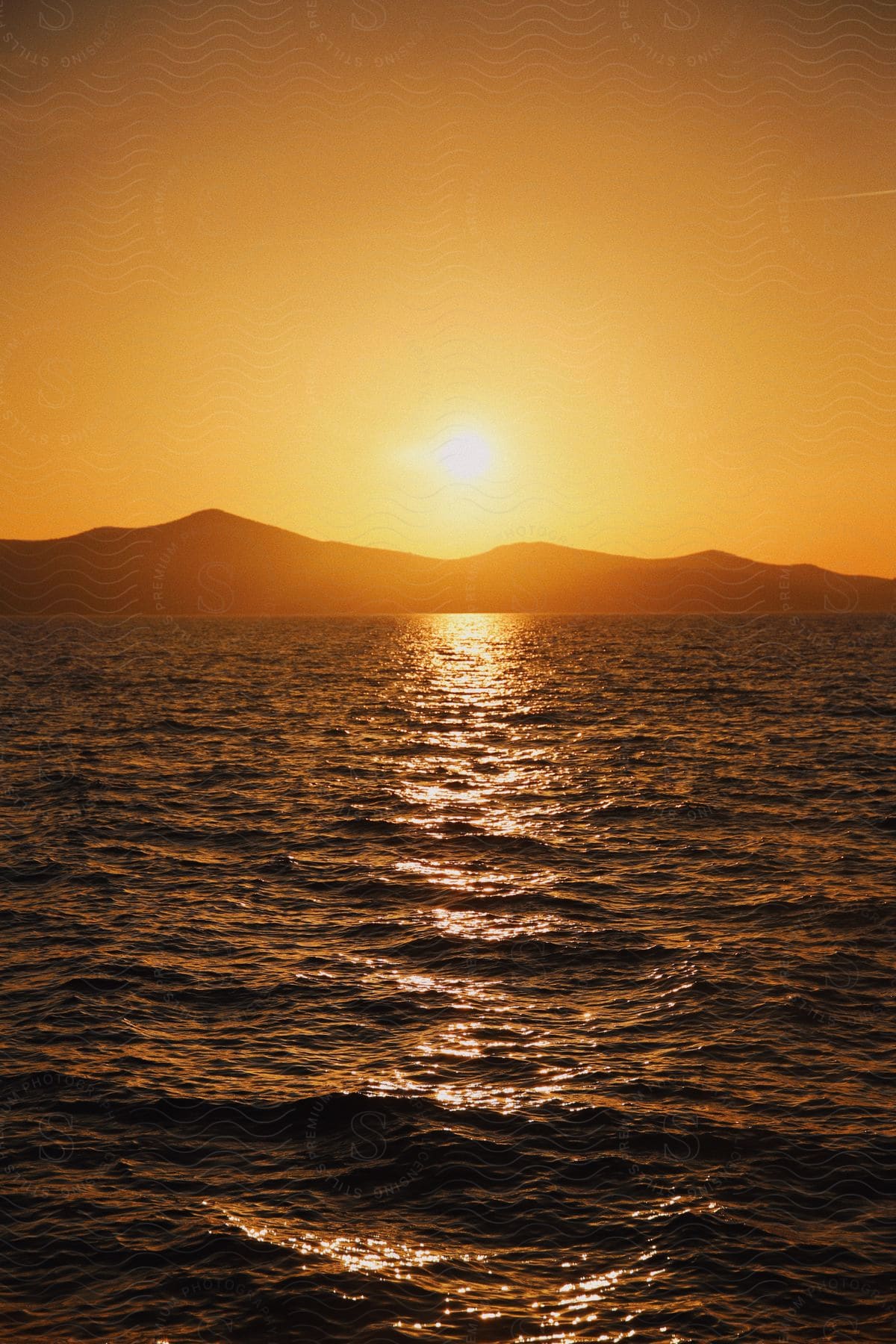 Sunset over the ocean with the sun casting a golden reflection on the water against a silhouette of mountains.