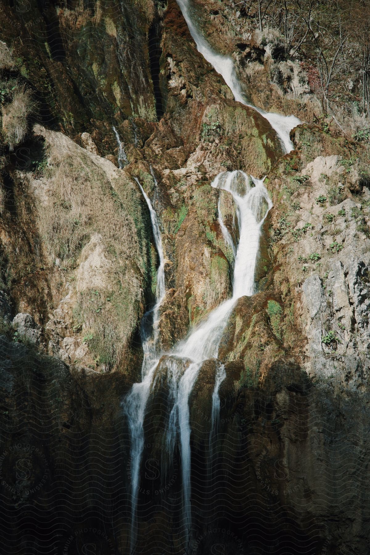 Water flows down rocky cliff with scattered plants and vegetation