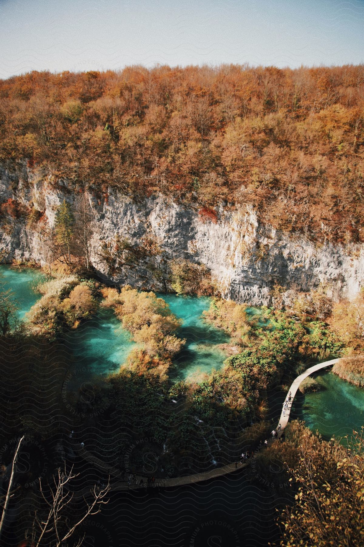 Stock photo of people walk on a bridge that winds over water along the coast of a forested mountain