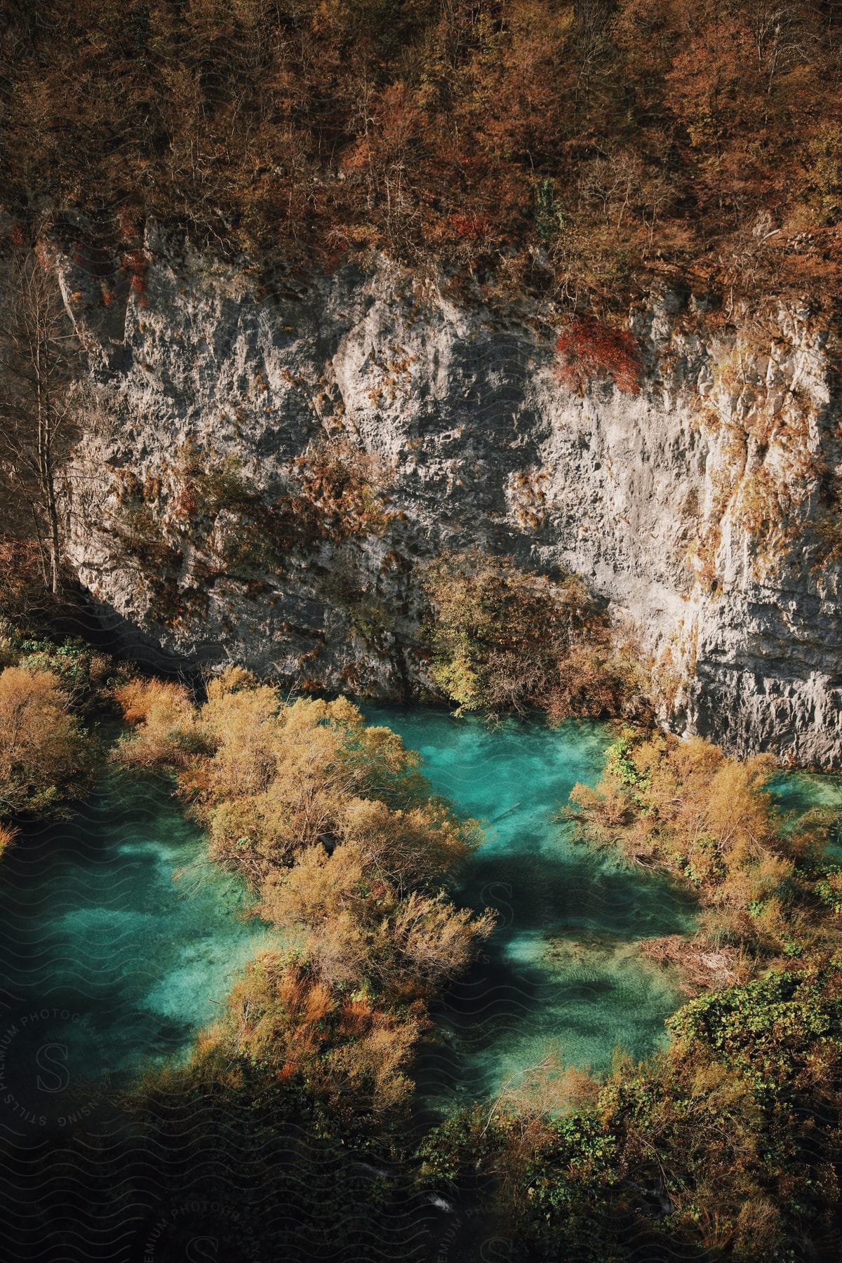 A light blue lake nestled in front of a rocky cliff, surrounded by an autumn forest