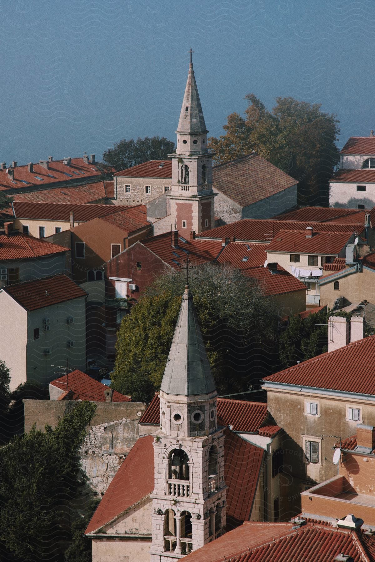 Aerial view of a historic church spire rising above terracotta rooftops in a quaint European town.