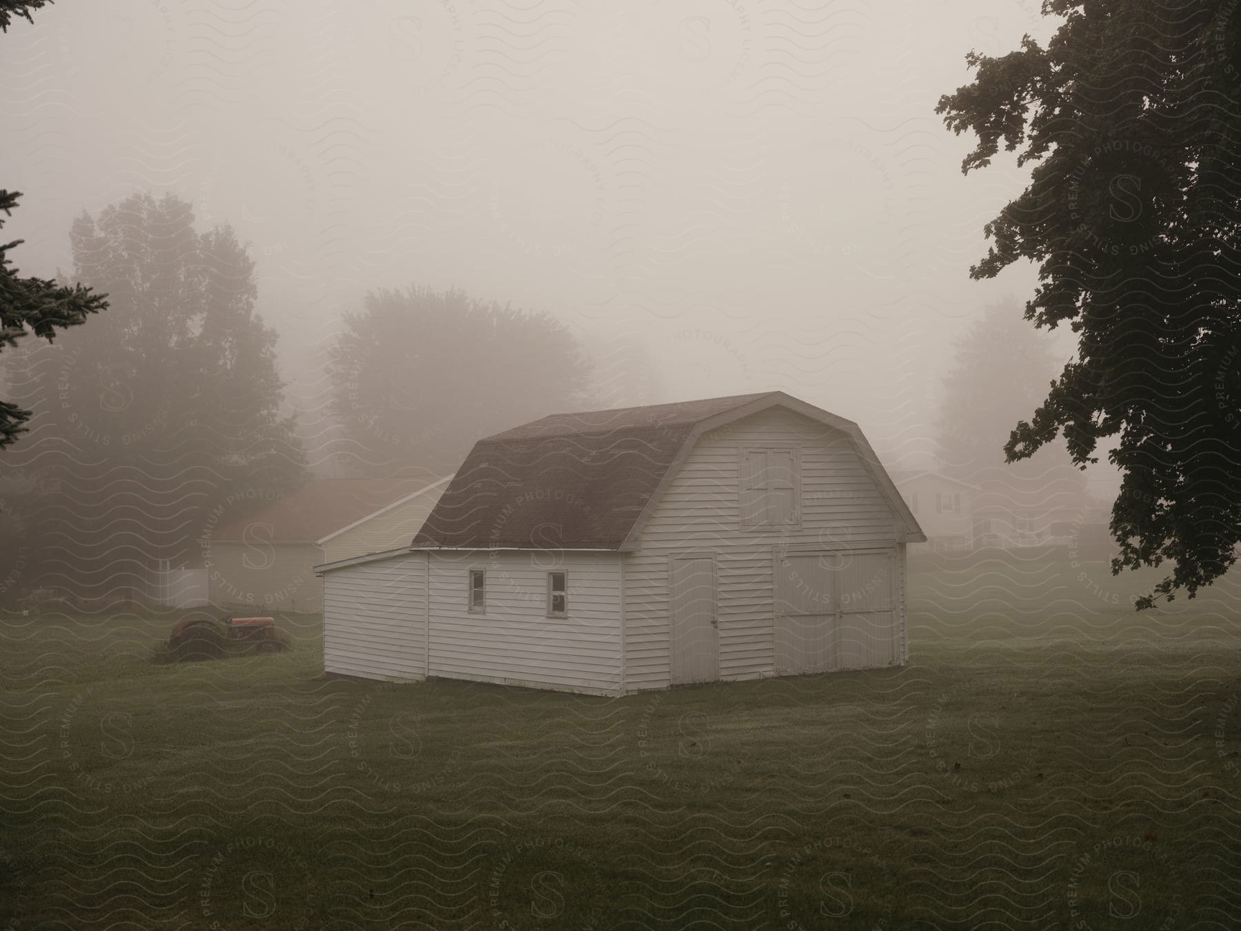 A barn house sits between trees in a foggy neighborhood