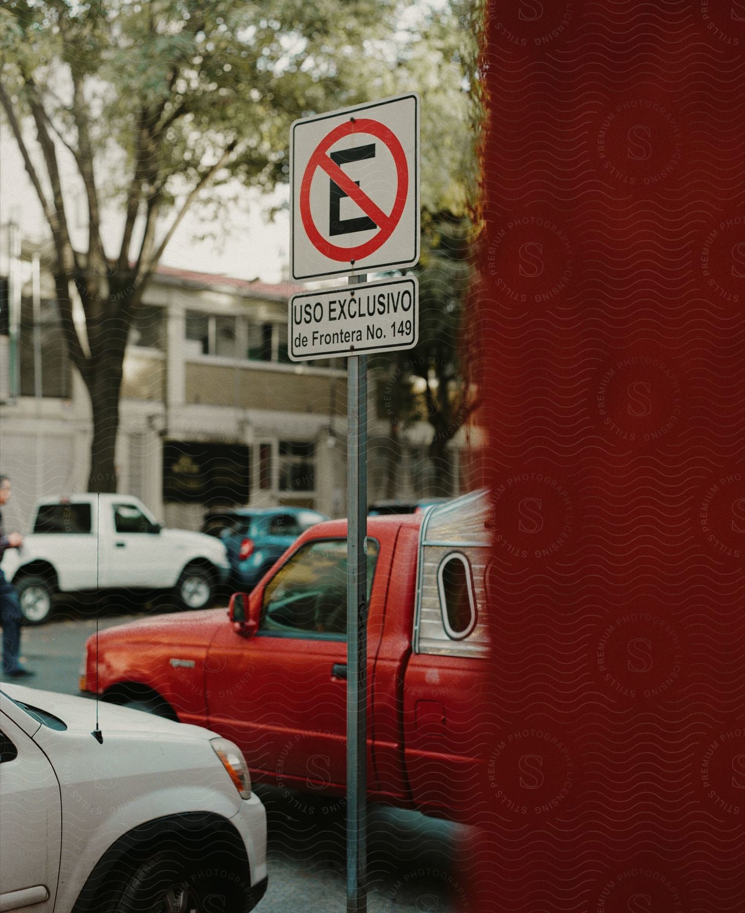 A man crosses the street while a red pick-up truck waits to make a turn near a parking sign.