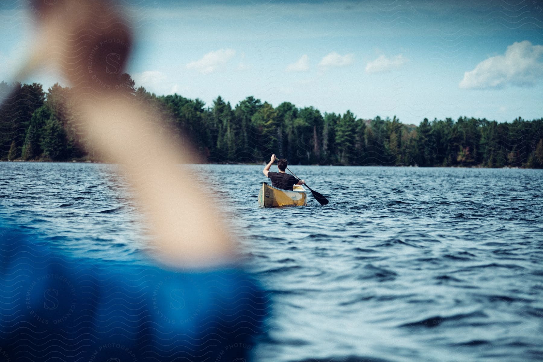 A person is in a canoe following close behind another canoe on the lake.