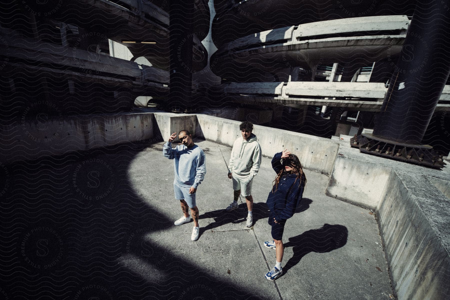 Three young adults stand in an empty parking lot while two of them have their hands in front of their faces.