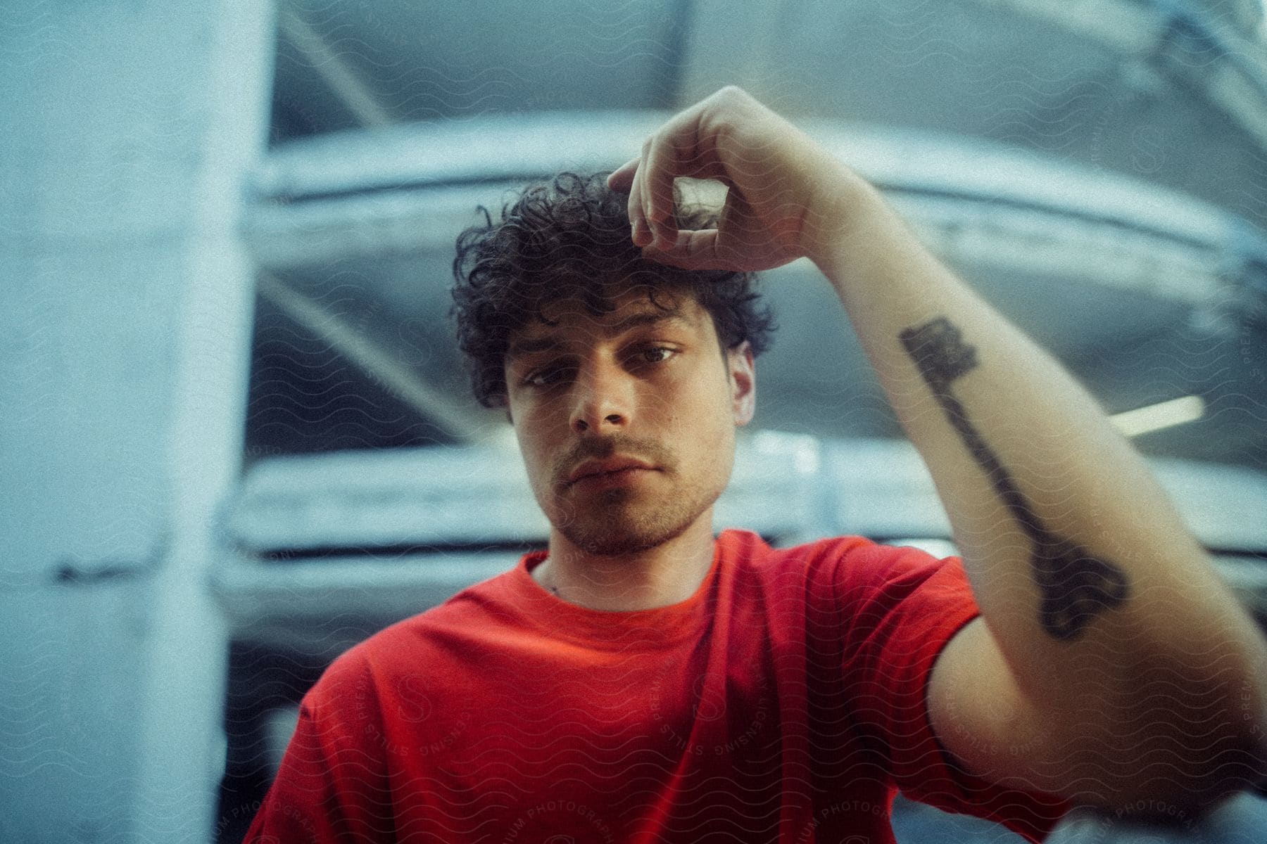 A young man wearing a red t-shirt and with a key tattoo on his left forearm is posing for the camera.