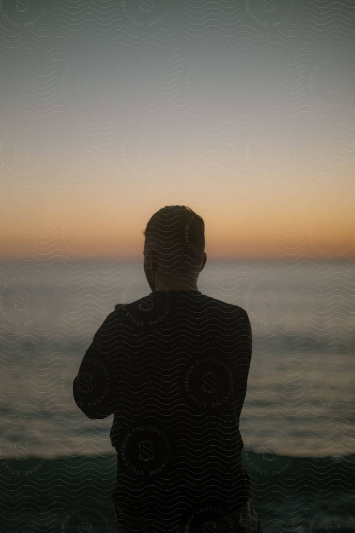 Silhouette of a person sitting in front of the ocean at evening