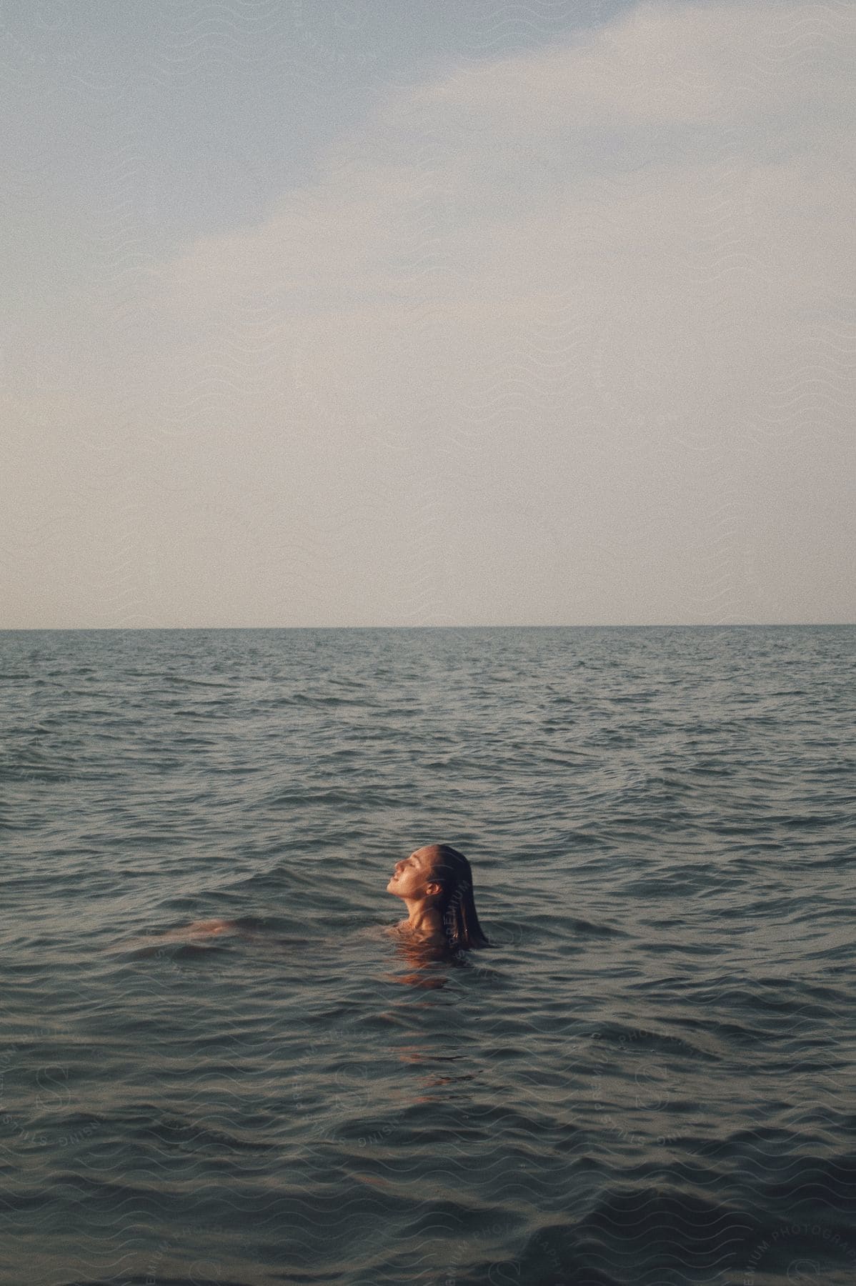 A young woman floats in the ocean under mostly cloudy skies.