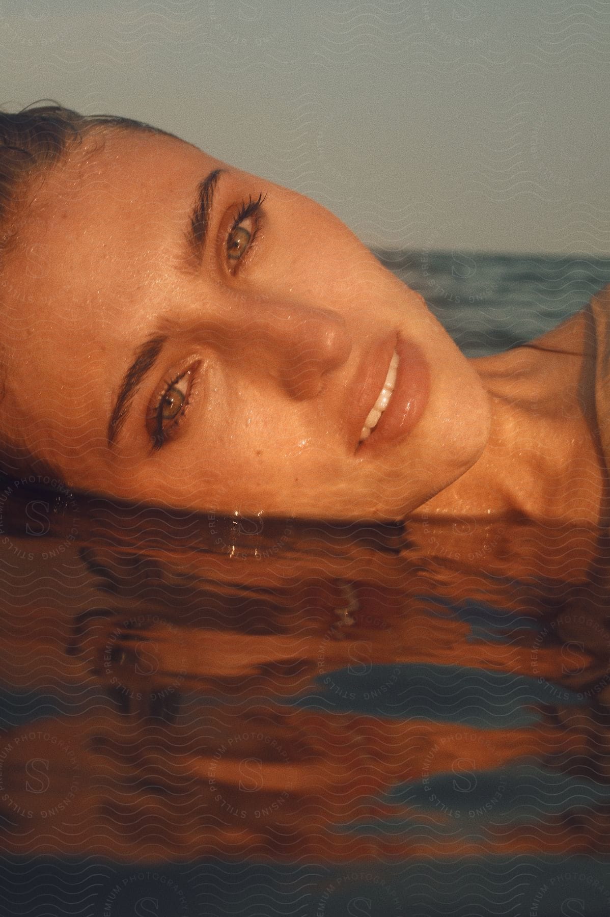 Woman modeling with her face submerged in the sea, her bright eyes visible on a cloudy day.