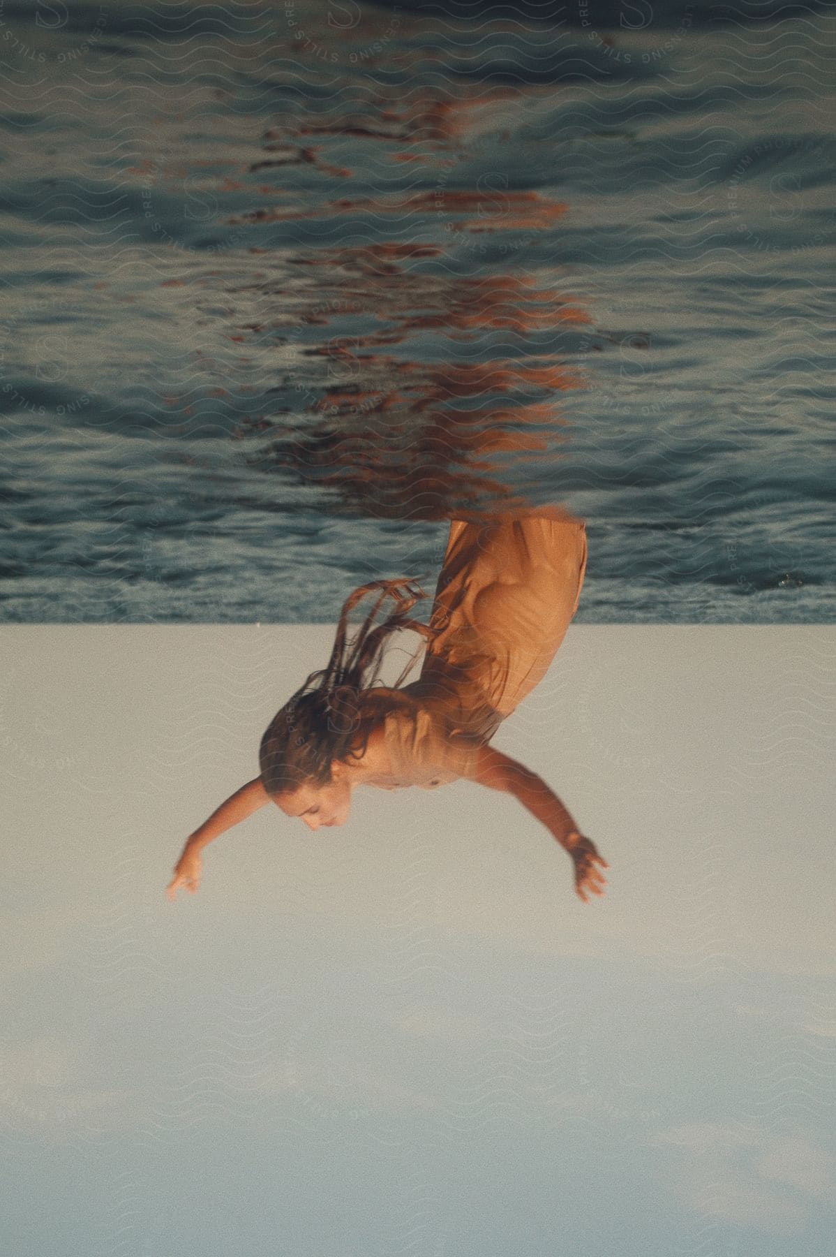 A woman is standing in the water with her back arched and her arms in the air as she falls backward