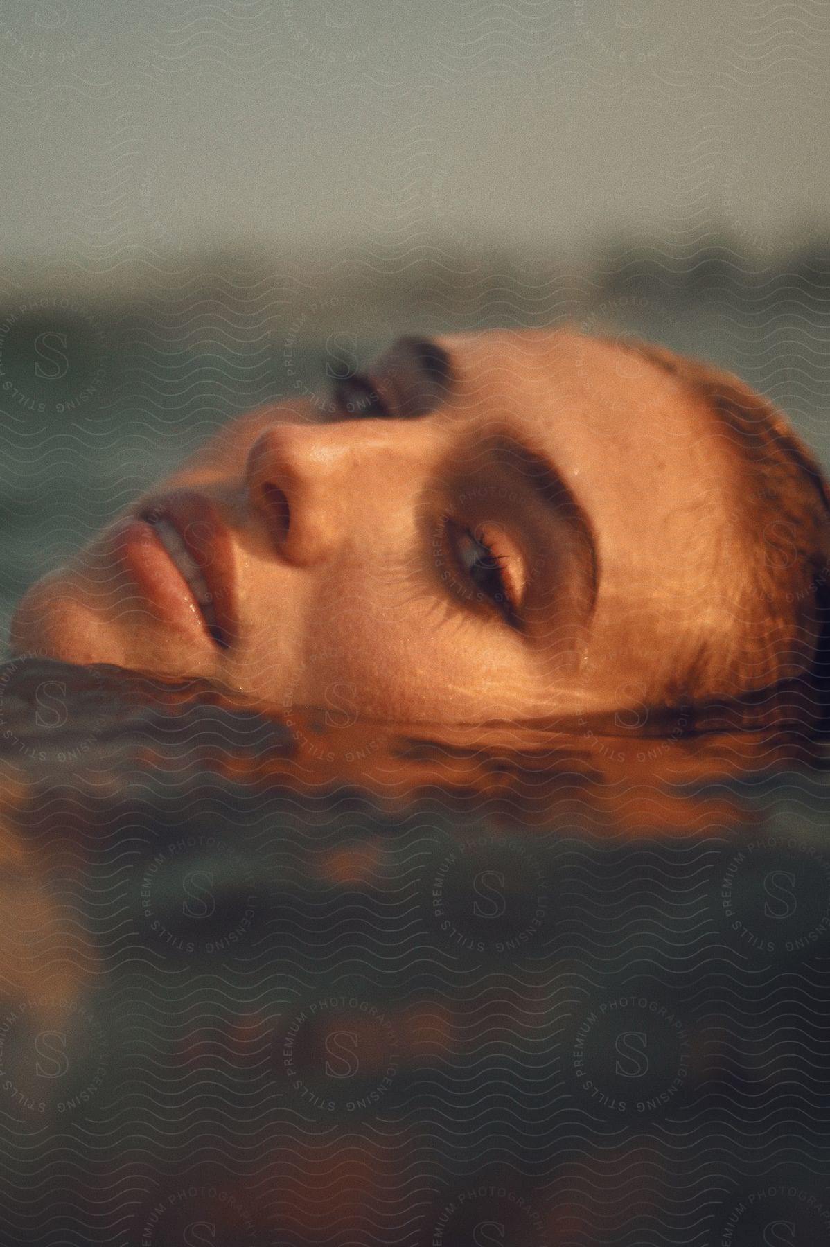 Close-up of a woman's face partially submerged in water, illuminated by golden sunlight.