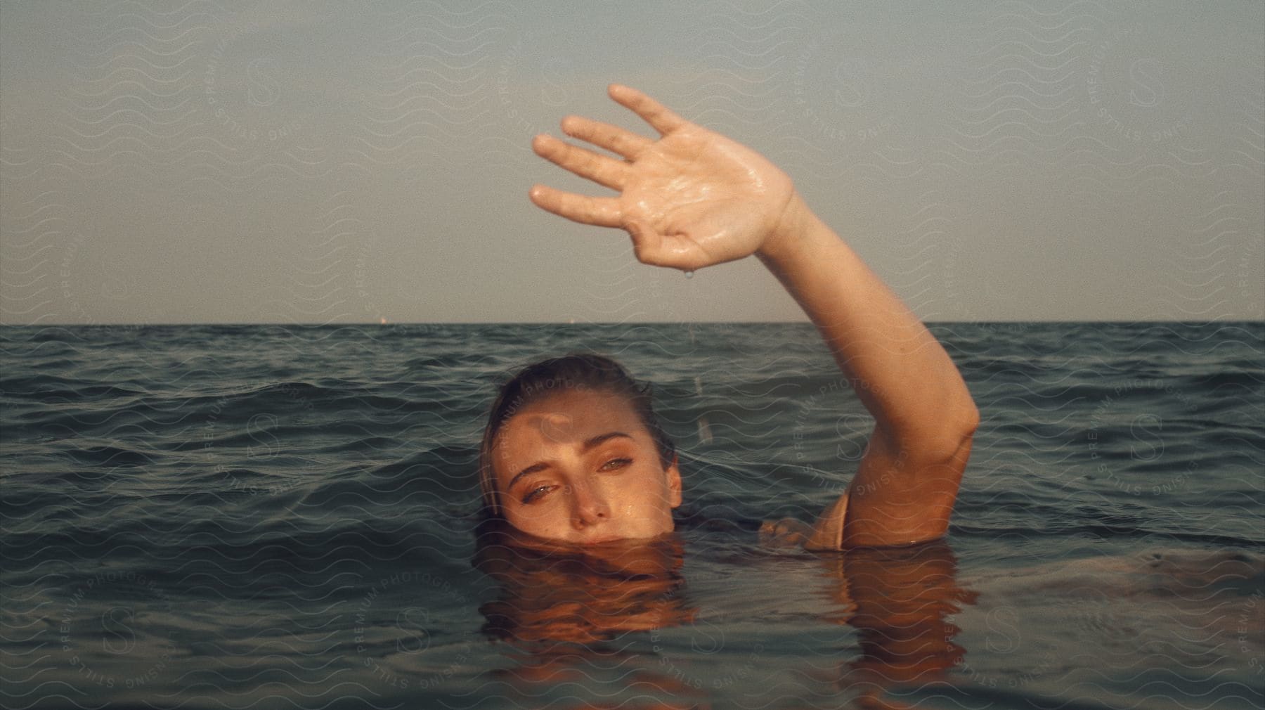 Woman mostly submerged in ocean water raises a hand.