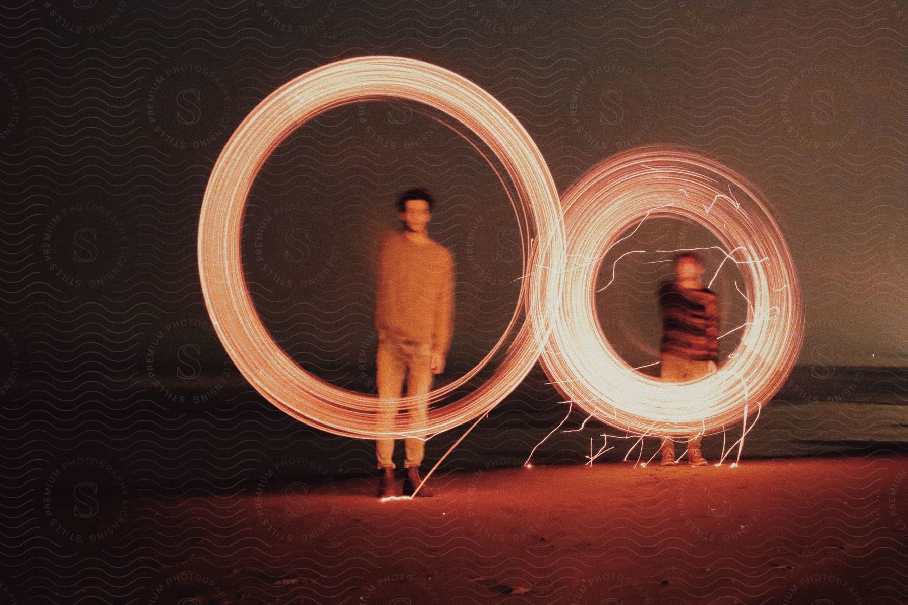 Two people on a beach at night creating light trails with a sparkler resulting in circular patterns of light.