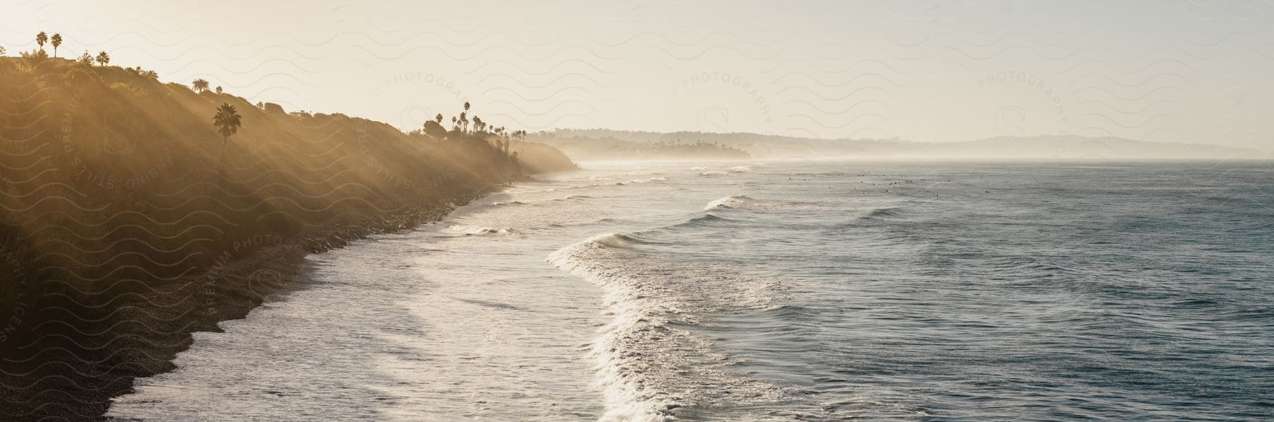 Panorama of a hill in front of a beach with solar reflection from the morning sun.