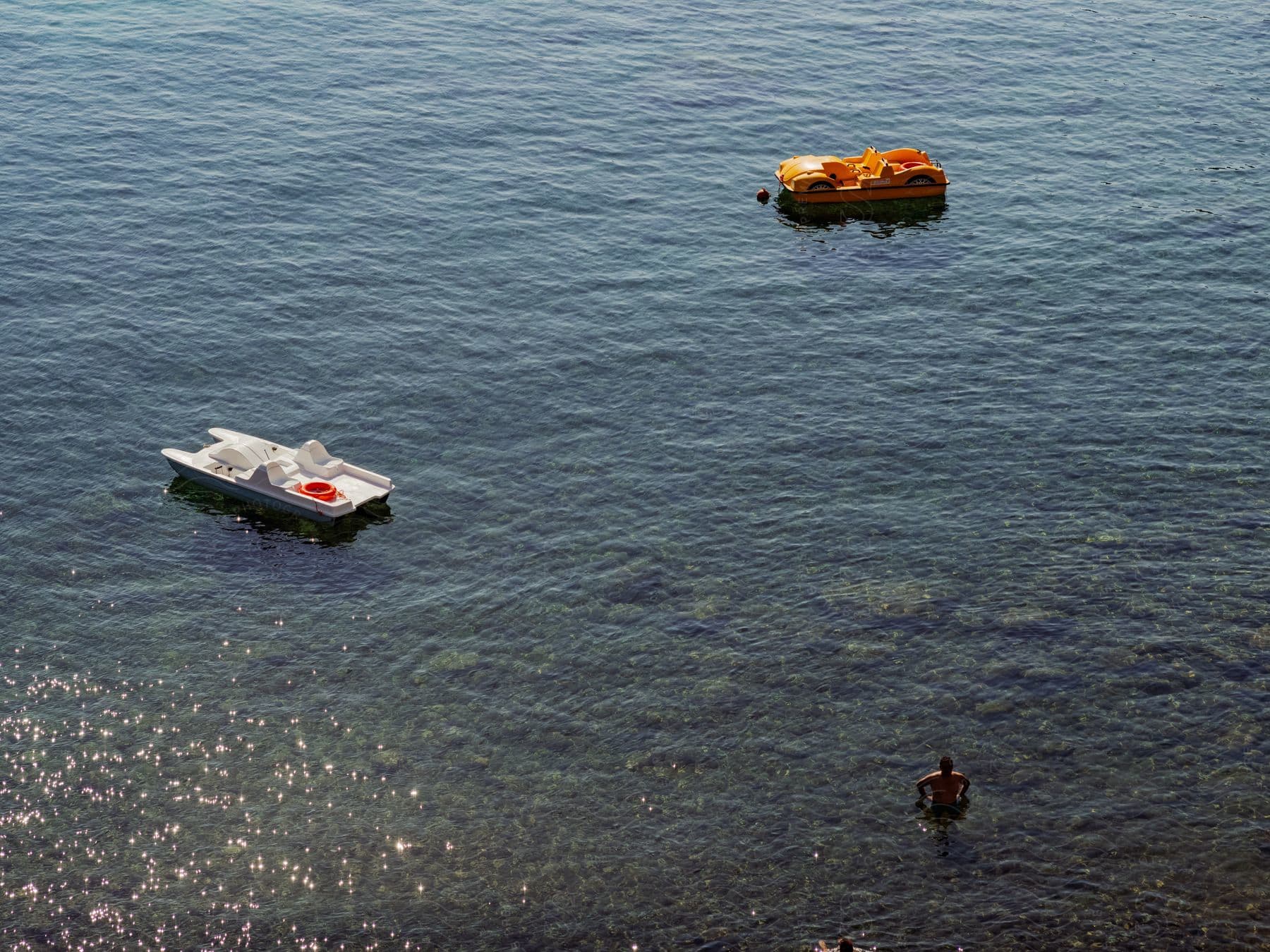 A man swims in the clear blue waters of the ocean near two anchored boats