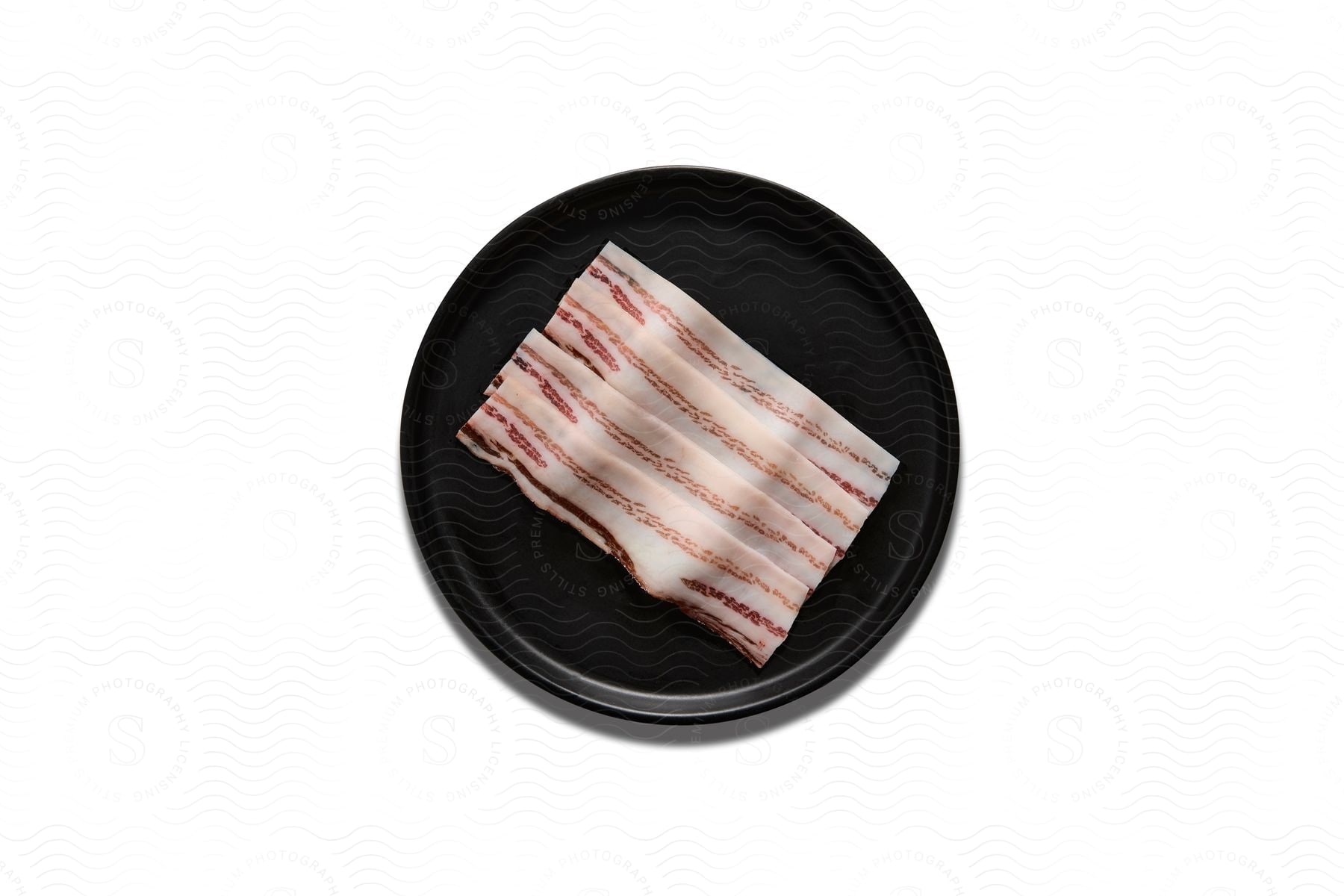 Raw Bacon Strips On A Black Plate Against A White Background