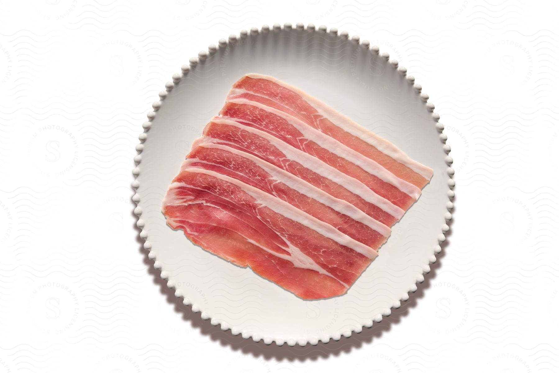 A plate of raw bacon slices on a white background with a white border around.