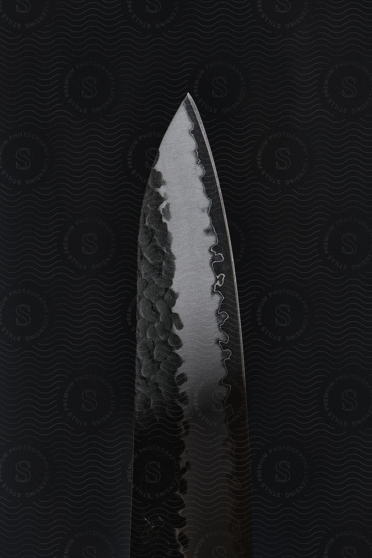 A close-up of a Damascus steel knife blade with a black background.