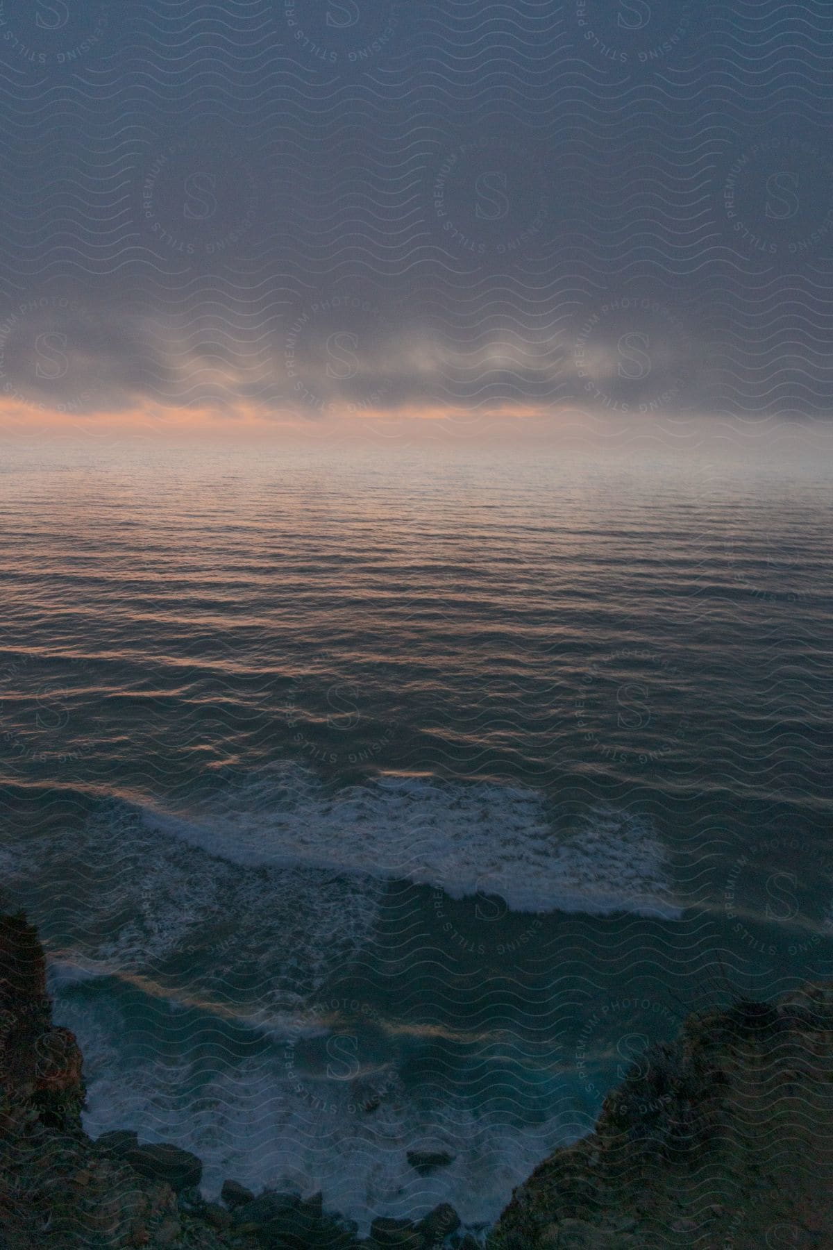 Top view of the coastline facing the sea with a cloudy dawn sky.