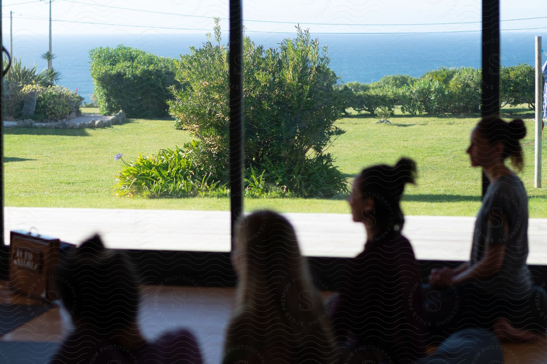 A group of women doing yoga in a living room with large glass windows in a house by the ocean.