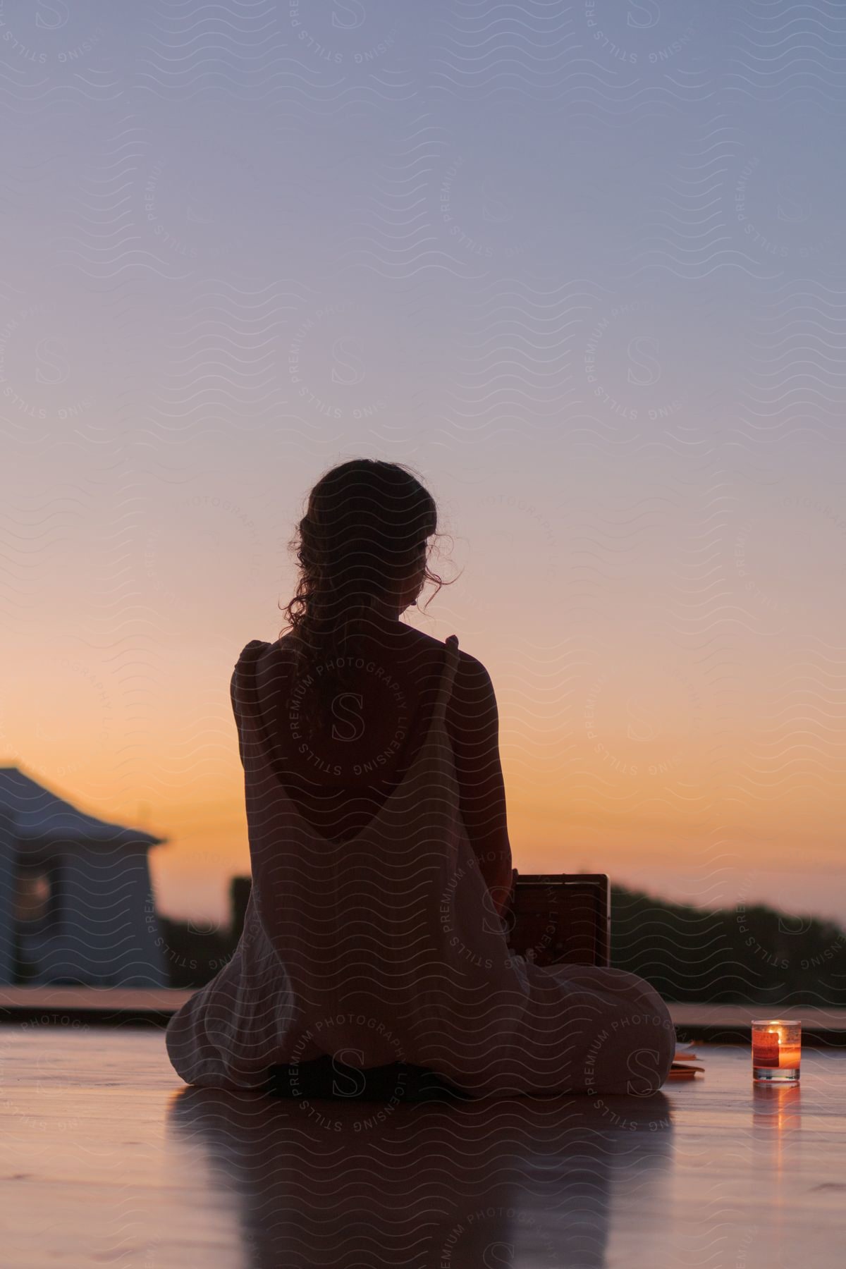 A woman is sitting on a balcony with a laptop computer and books with a candle