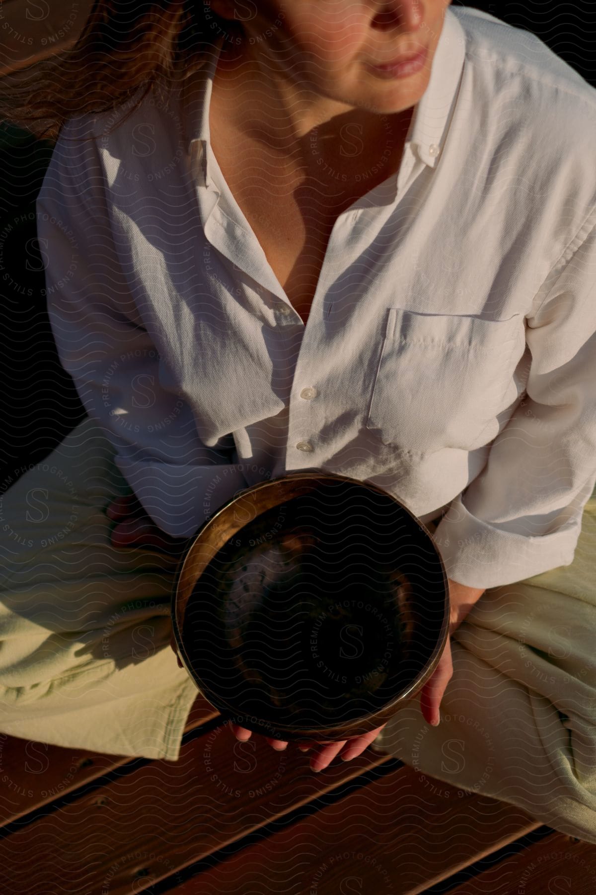 A woman is sitting on a deck with a meditation bowl in her hands
