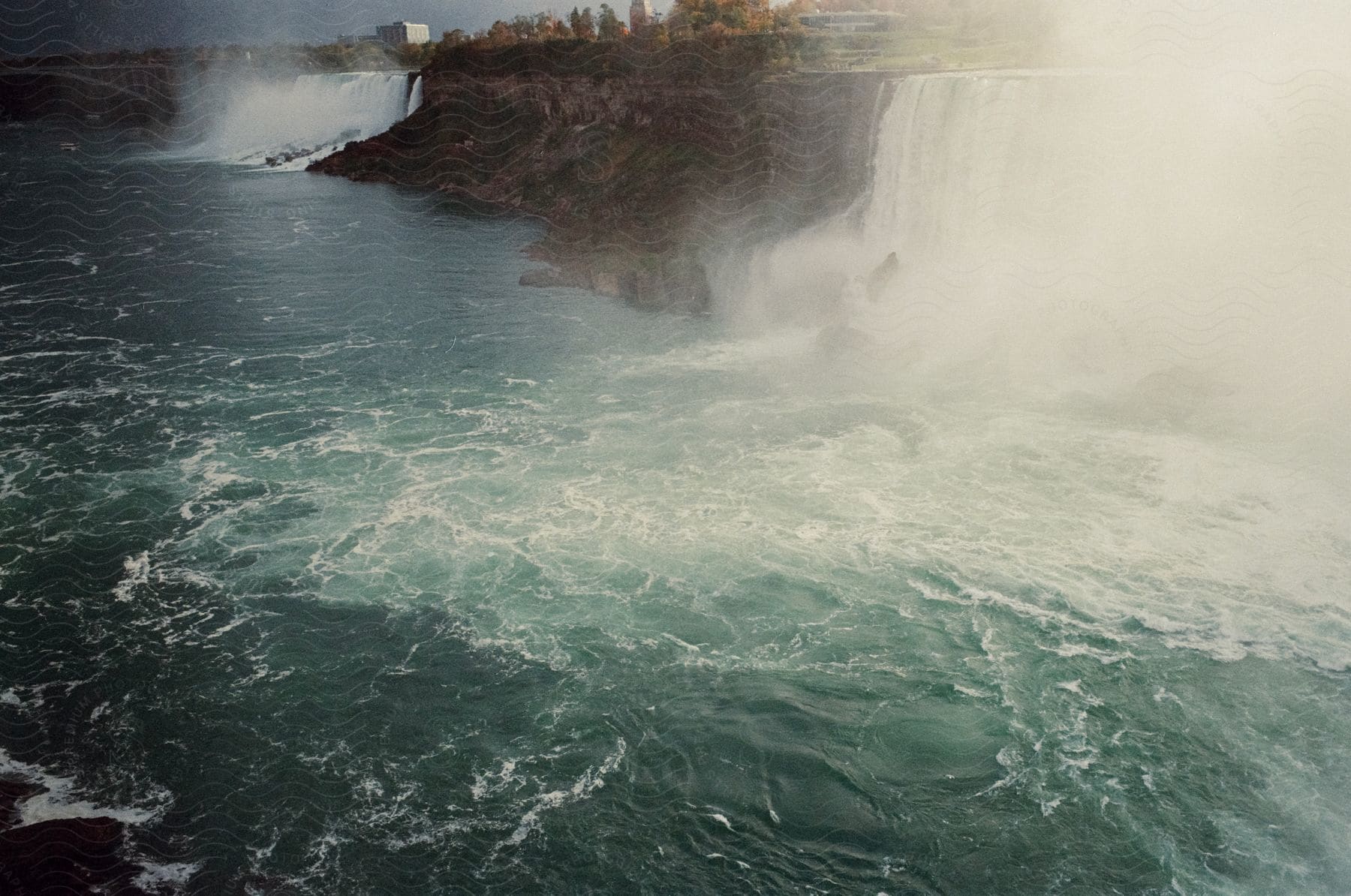 The landscape of Niagara Falls features the powerful rush of water over the cliffs, surrounded by mist