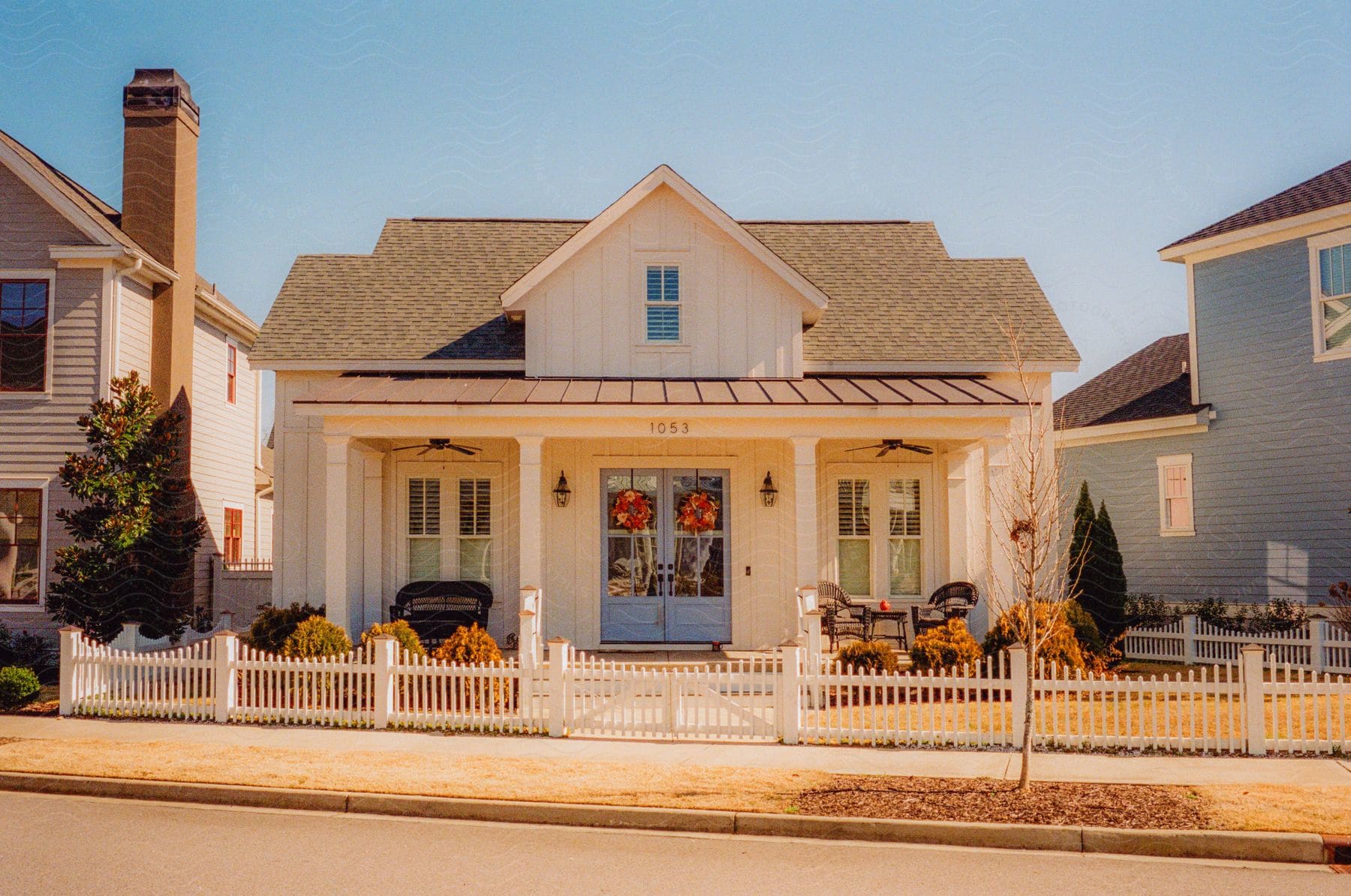 A house with white picket fence and a front porch with wreaths hanging on the double front door