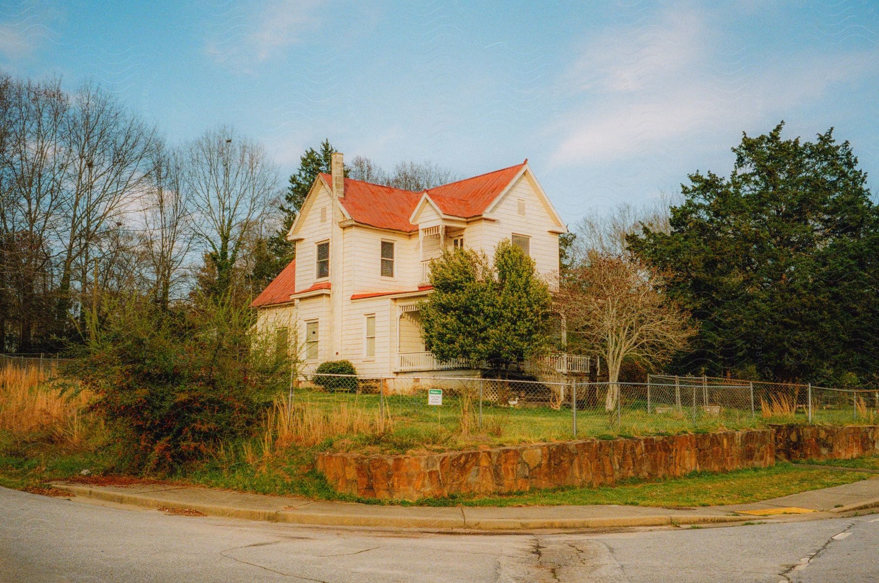 A big house with a chain link fence around the property on a neighborhood corner surrounded by trees