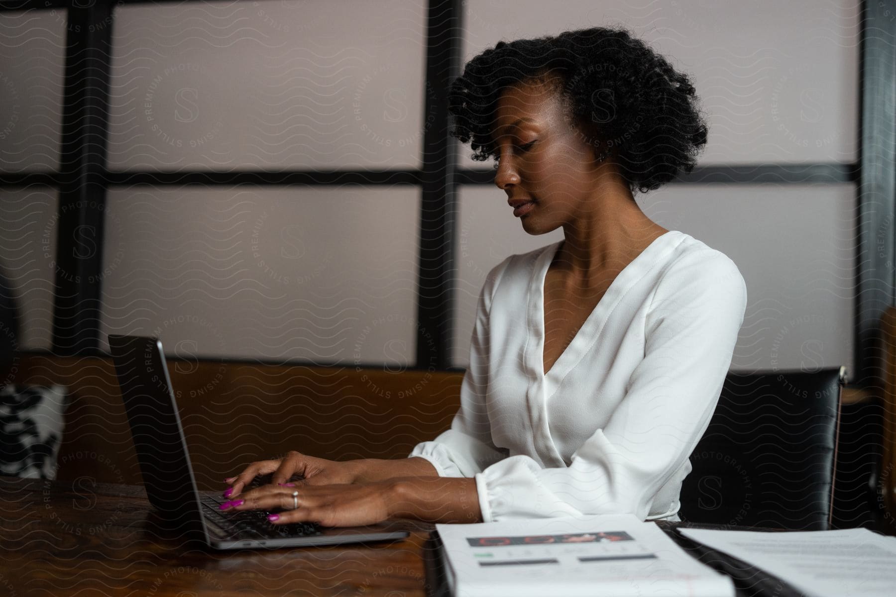 A woman is sitting at a desk typing on a laptop computer with books next to her