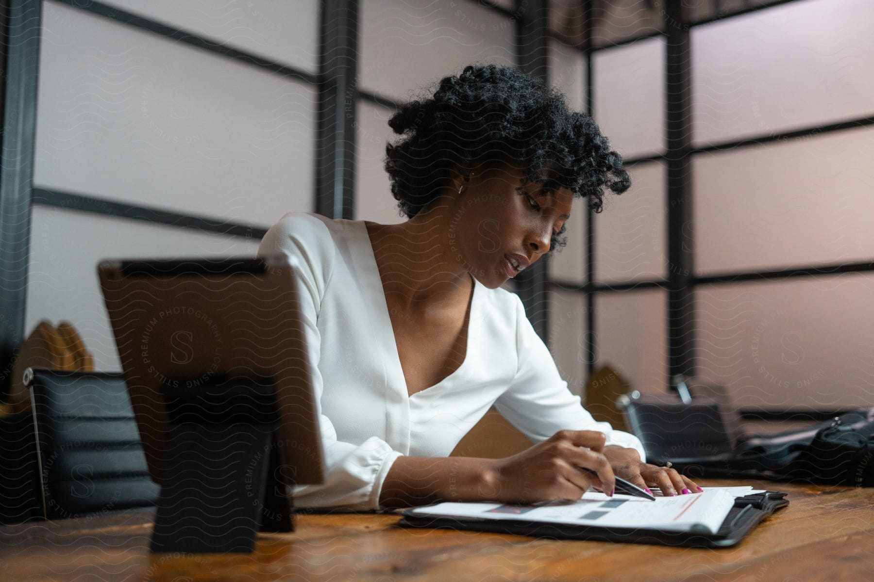 A woman is sitting at a desk in her office looking over paperwork with a pen in her hand