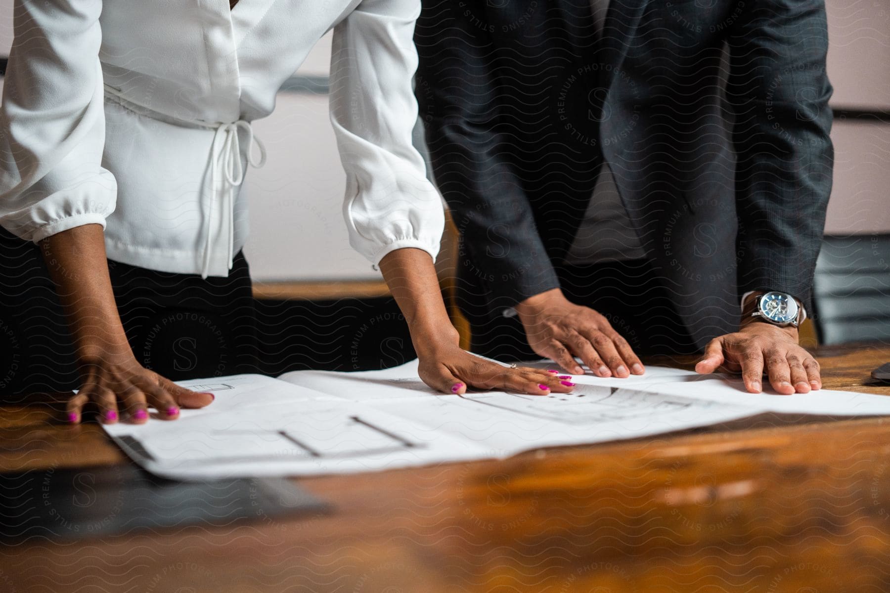 A man and a women are standing over their desk looking at a large piece of paper.